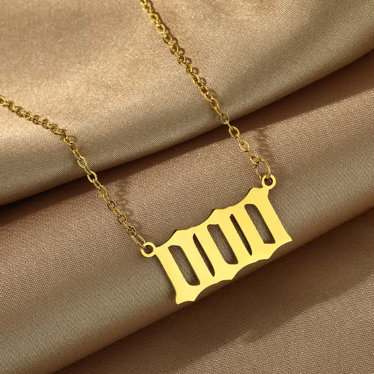 A gold angel number 000 necklace displayed on soft, golden satin fabric. The pendant has a bold, modern cut-out design, representing alignment, manifestation, and new beginnings. The delicate gold ch