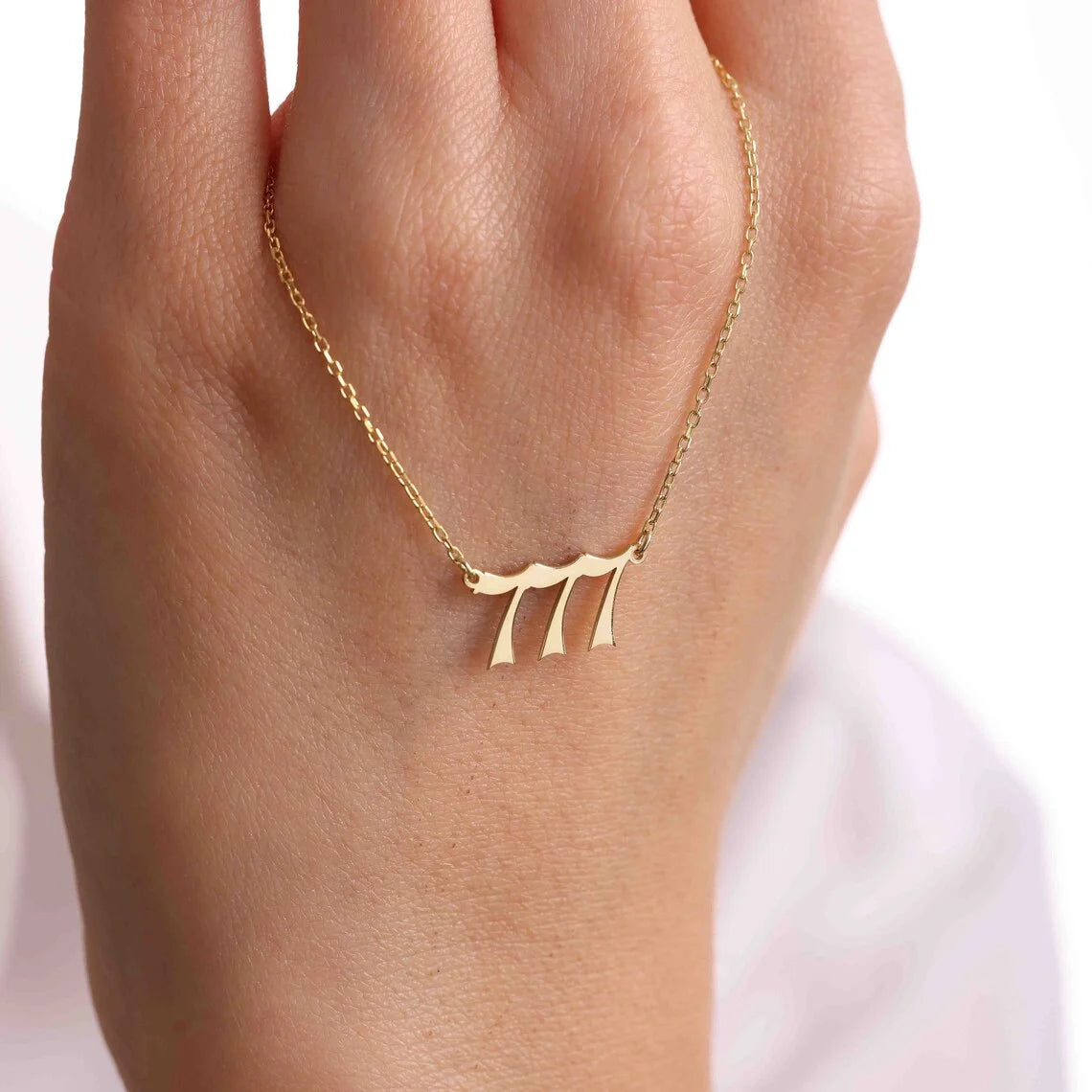 A close-up of a hand holding a gold angel number 777 necklace, showcasing its elegant and polished number design.