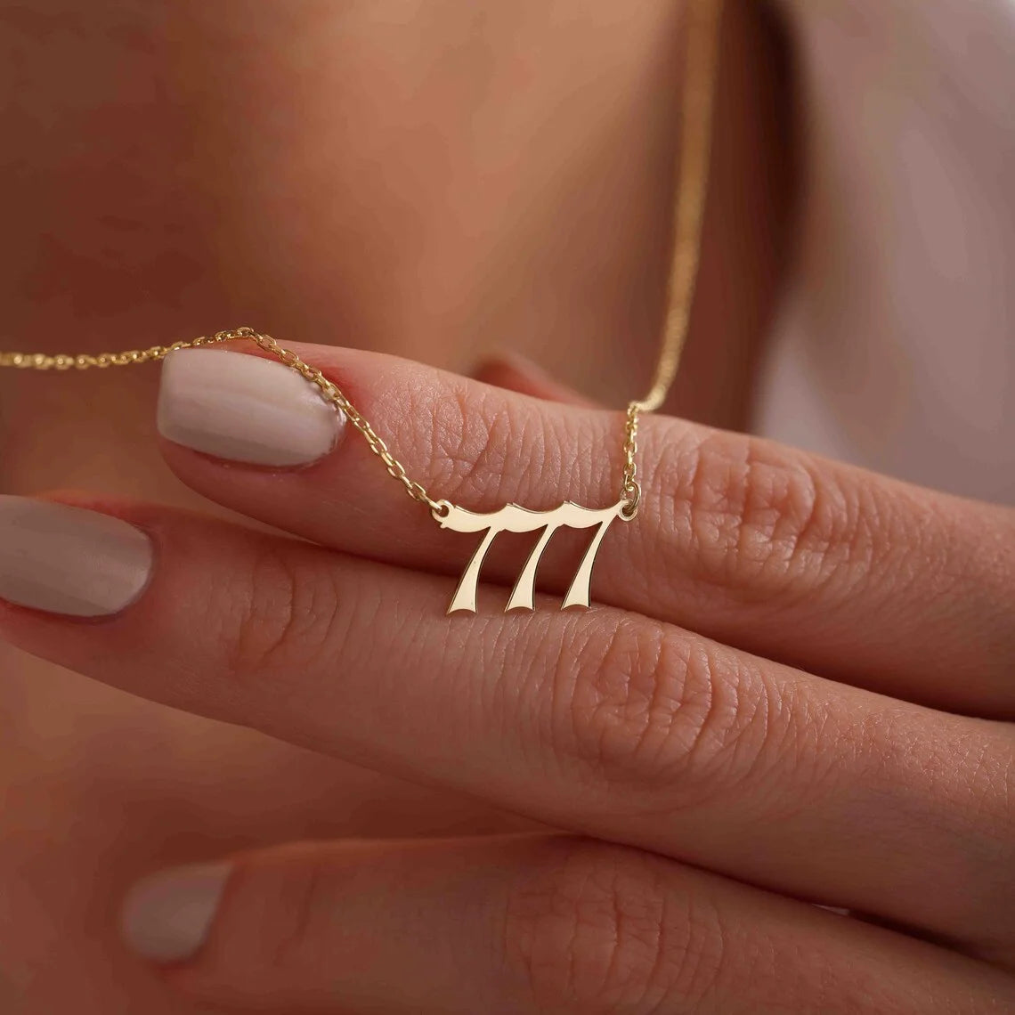 A detailed shot of the angel number 777 necklace draped over fingers, emphasizing the smooth gold pendant and fine chain.