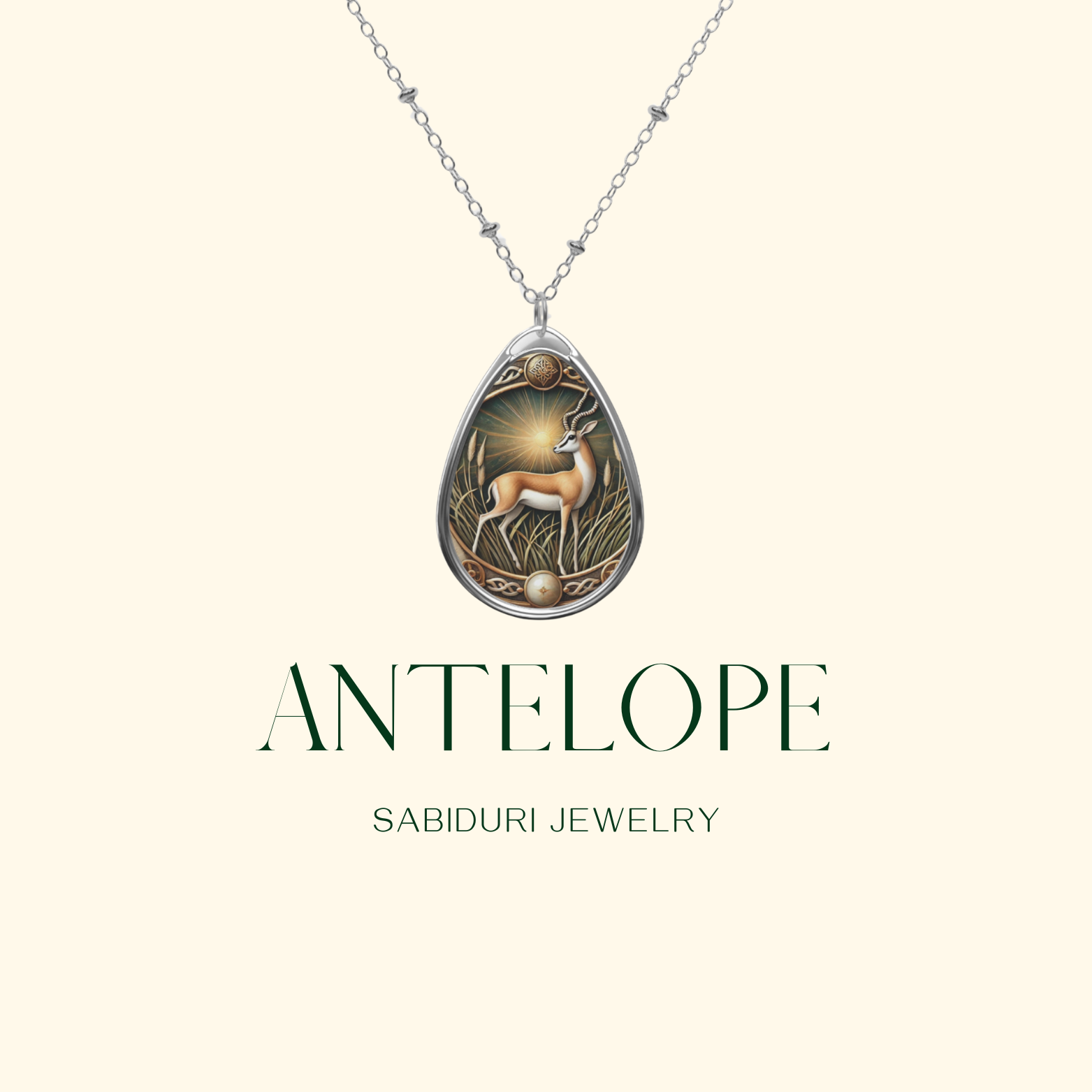 A delicate silver necklace with a teardrop-shaped pendant showcasing an antelope gracefully posed in a golden field. The pendant is displayed on a neutral background, with the text "ANTELOPE" and "SABIDURI JEWELRY" elegantly positioned beneath.