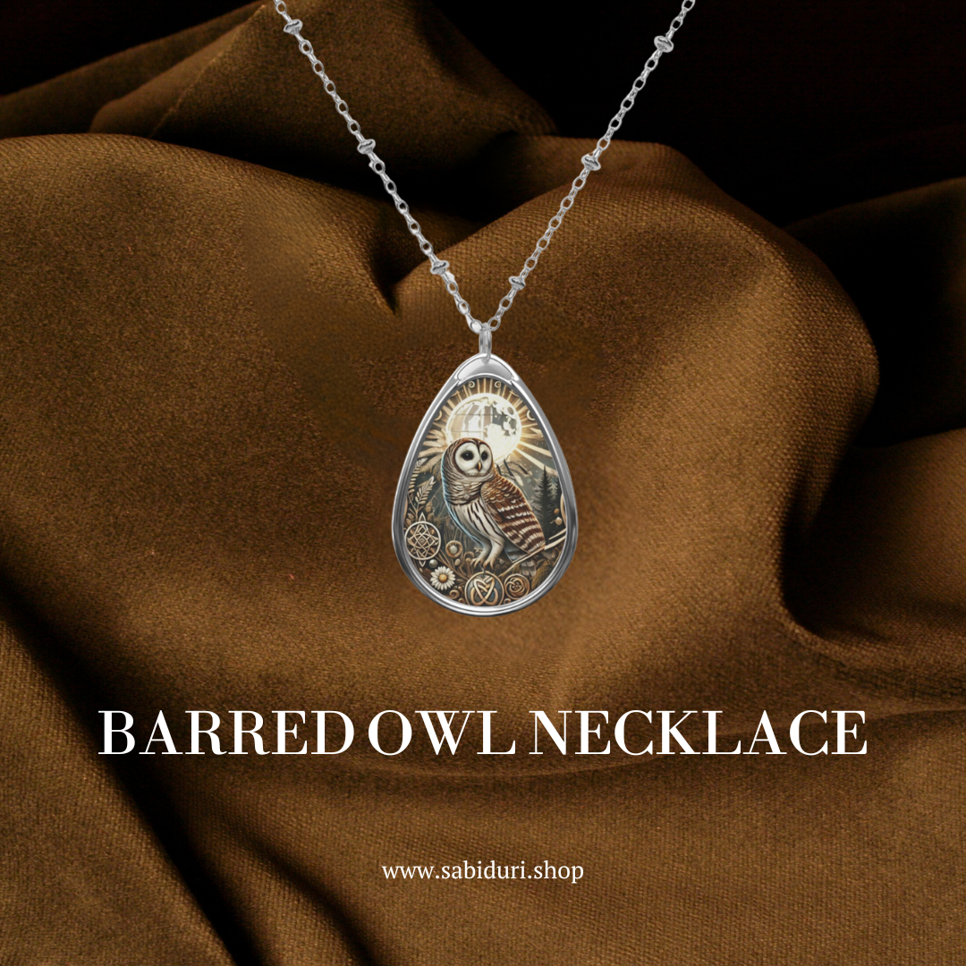  A Barred Owl necklace with a silver chain, displayed on a rich brown fabric. The pendant is teardrop-shaped, featuring an intricately designed owl, with the text "BARRED OWL NECKLACE" and the website "www.sabiduri.shop" below it.