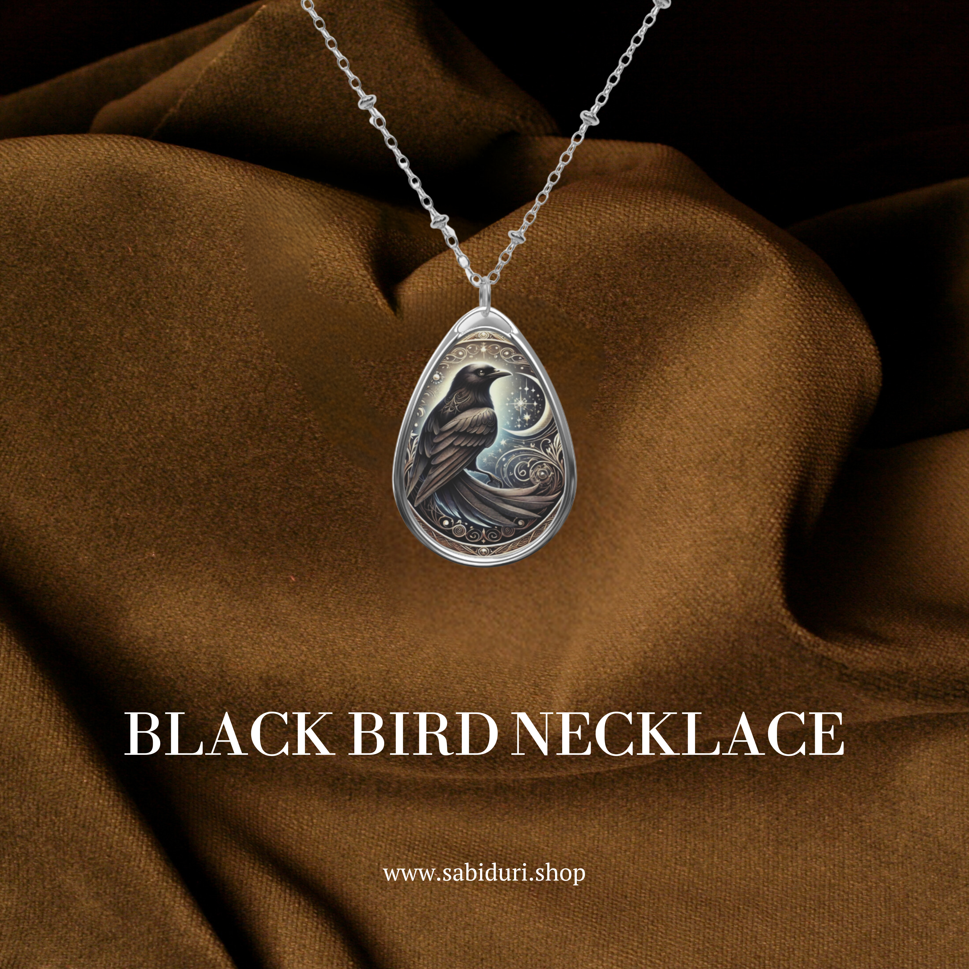 The Black Bird Spirit Animal Necklace elegantly laid on rich brown fabric, showcasing the pendant's intricate celestial detailing and deep-toned engraving of the bird. The words "Black Bird Necklace" and "www.sabiduri.shop" are included in the design.