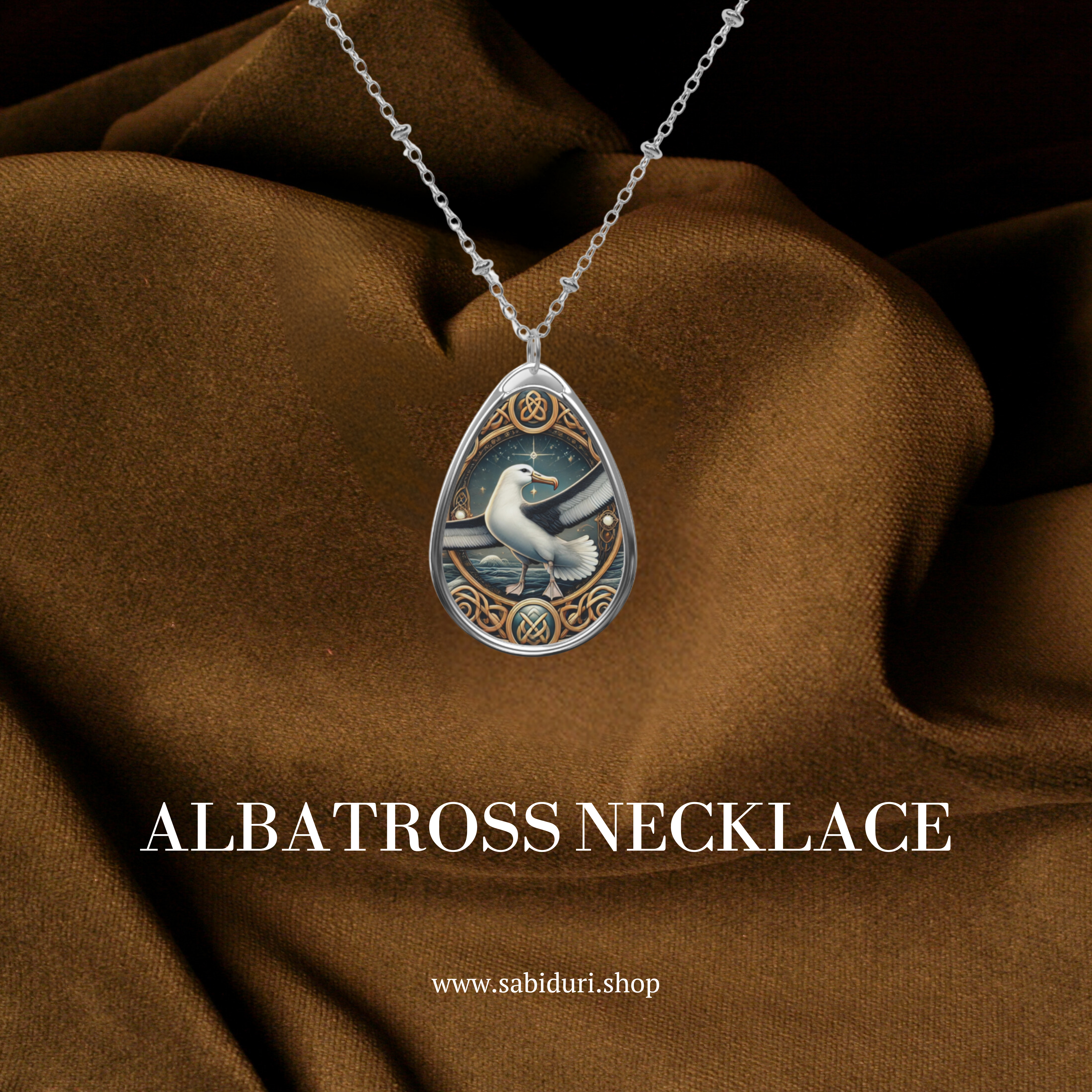 A silver albatross pendant necklace with ornate engravings, featuring a majestic albatross in flight against a deep blue ocean-inspired background. The pendant is displayed against a rich brown fabric backdrop, with the text "ALBATROSS NECKLACE" and the website "www.sabiduri.shop" below.