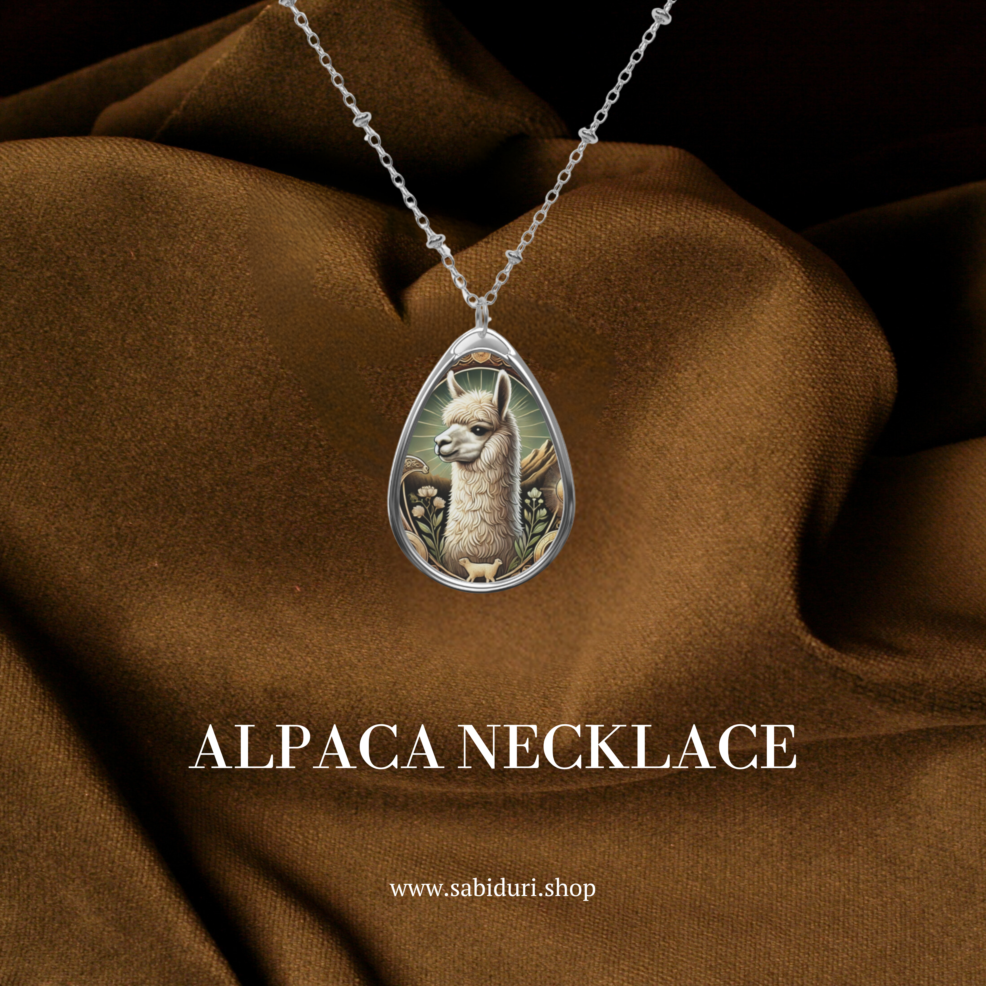 A silver alpaca pendant necklace with ornate engravings, depicting a detailed alpaca in a natural setting with delicate floral and earthy accents. The pendant is displayed against a luxurious brown fabric background, with the text "ALPACA NECKLACE" and the website "www.sabiduri.shop" below.