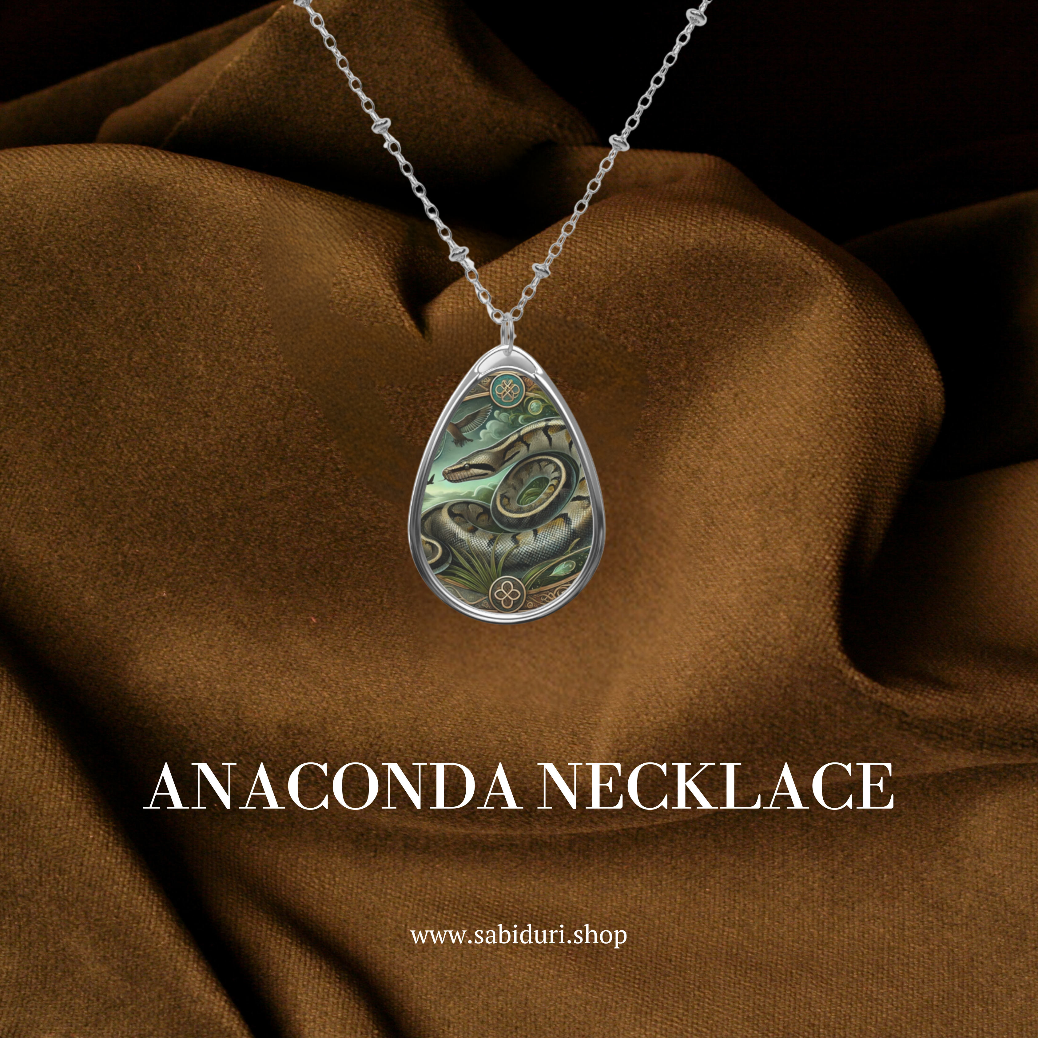 A silver anaconda pendant necklace with detailed engravings, featuring a coiled snake set against a deep green rainforest-inspired background. The pendant is displayed against a rich brown fabric backdrop, with the text "ANACONDA NECKLACE" and the website "www.sabiduri.shop" below.