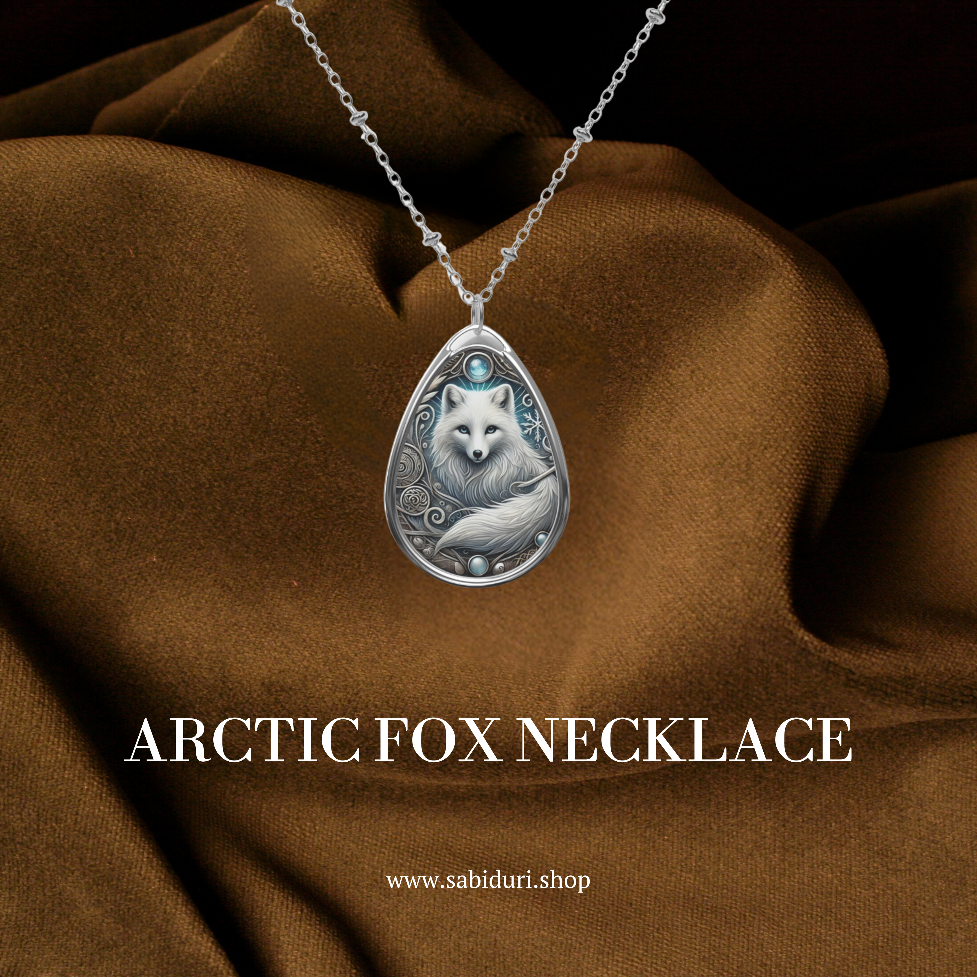 A silver Arctic fox pendant necklace with ornate, swirling engravings and icy blue gemstones. The pendant is displayed against a rich brown fabric background, with the text "ARCTIC FOX NECKLACE" and the website "www.sabiduri.shop" below.