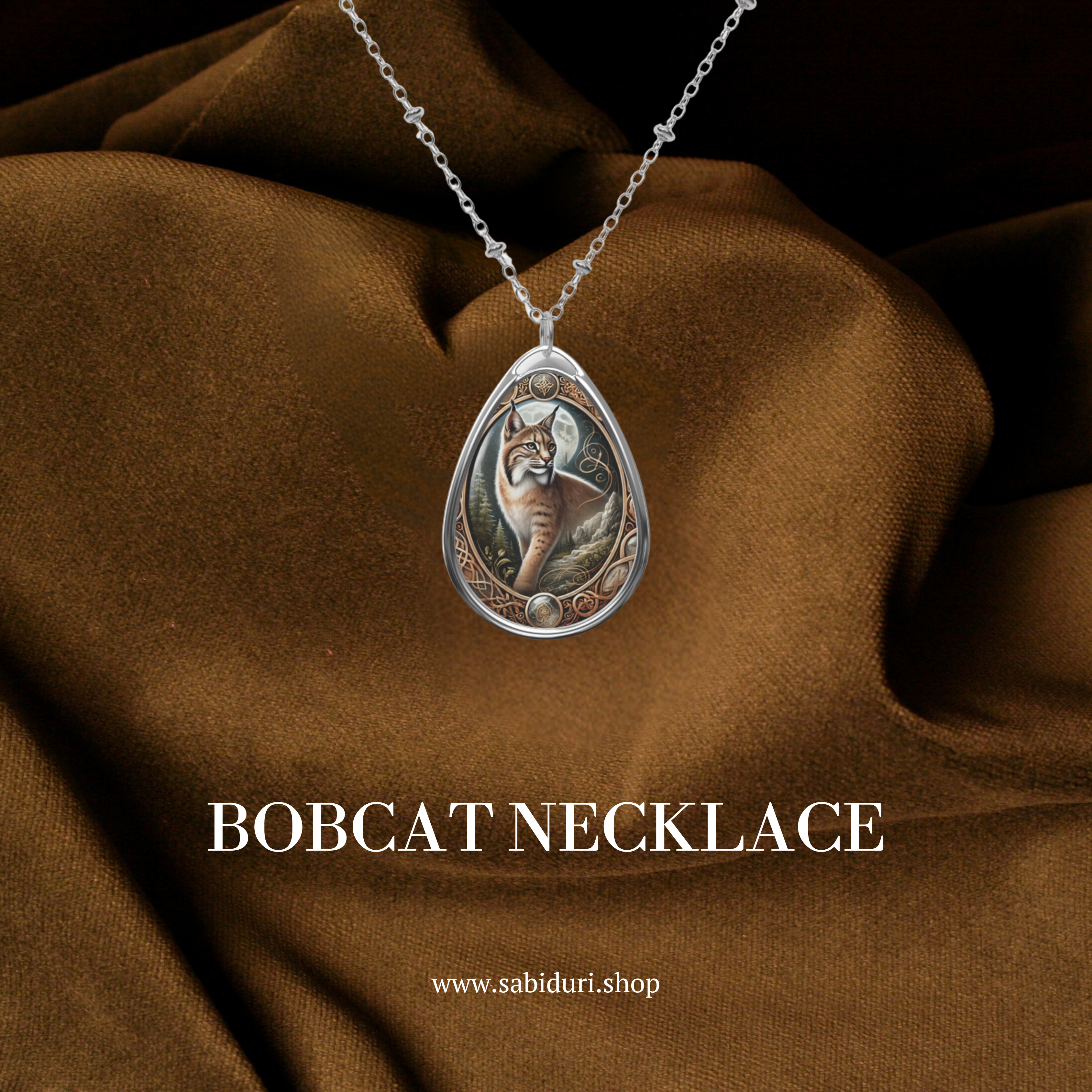 A close-up of the bobcat necklace against a luxurious brown fabric backdrop. The pendant showcases a detailed bobcat standing in a natural setting, framed with ornate golden accents. Below, the text "BOBCAT NECKLACE" and "www.sabiduri.shop" add branding.