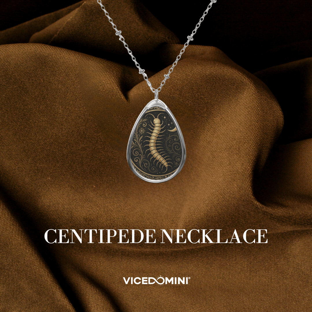 Centipede necklace with ornate golden detailing showcased against rich brown fabric, with the text “CENTIPEDE NECKLACE”.