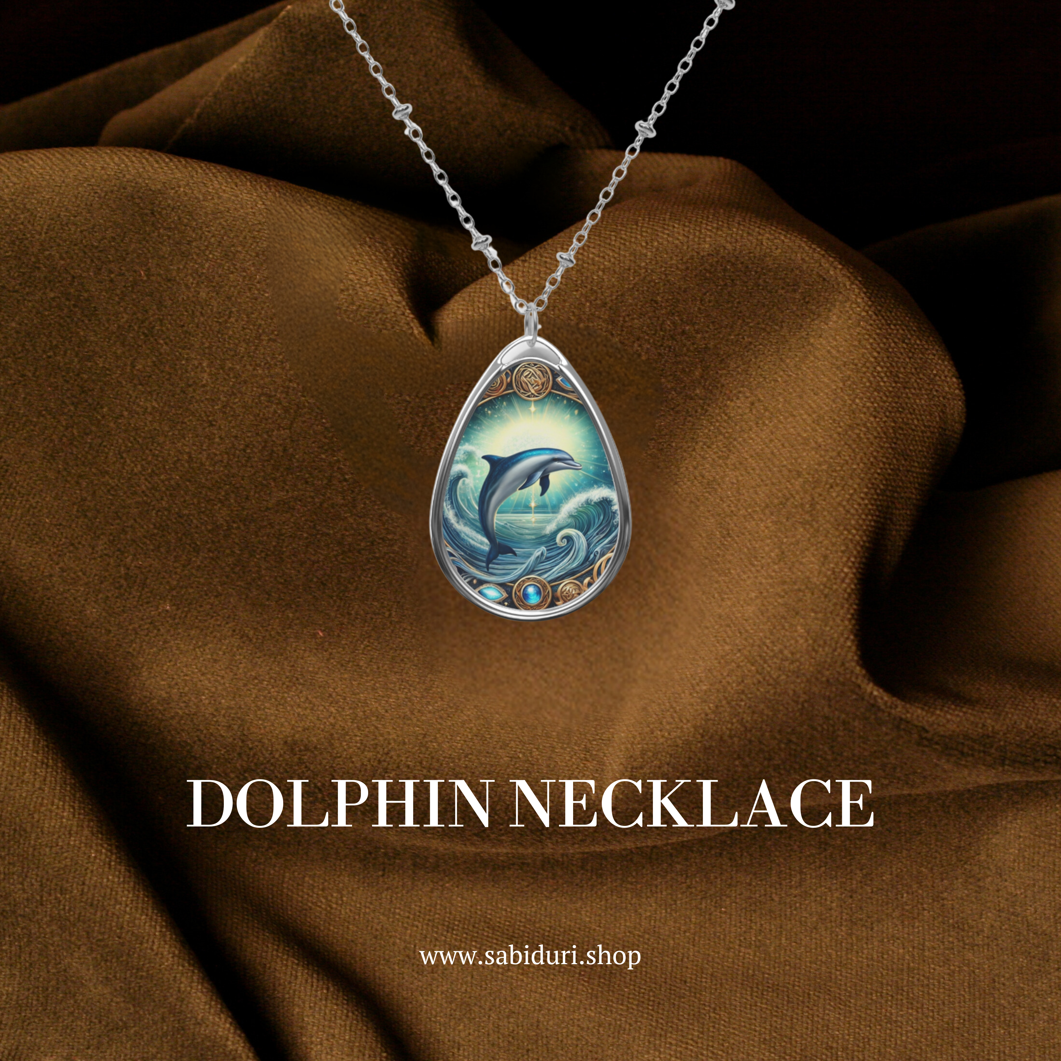 A close-up of a Dolphin spirit animal necklace against a rich brown fabric backdrop. The silver pendant showcases a leaping dolphin surrounded by swirling waves and ornate gold details. The text "DOLPHIN NECKLACE" and "www.sabiduri.shop" are displayed in white.