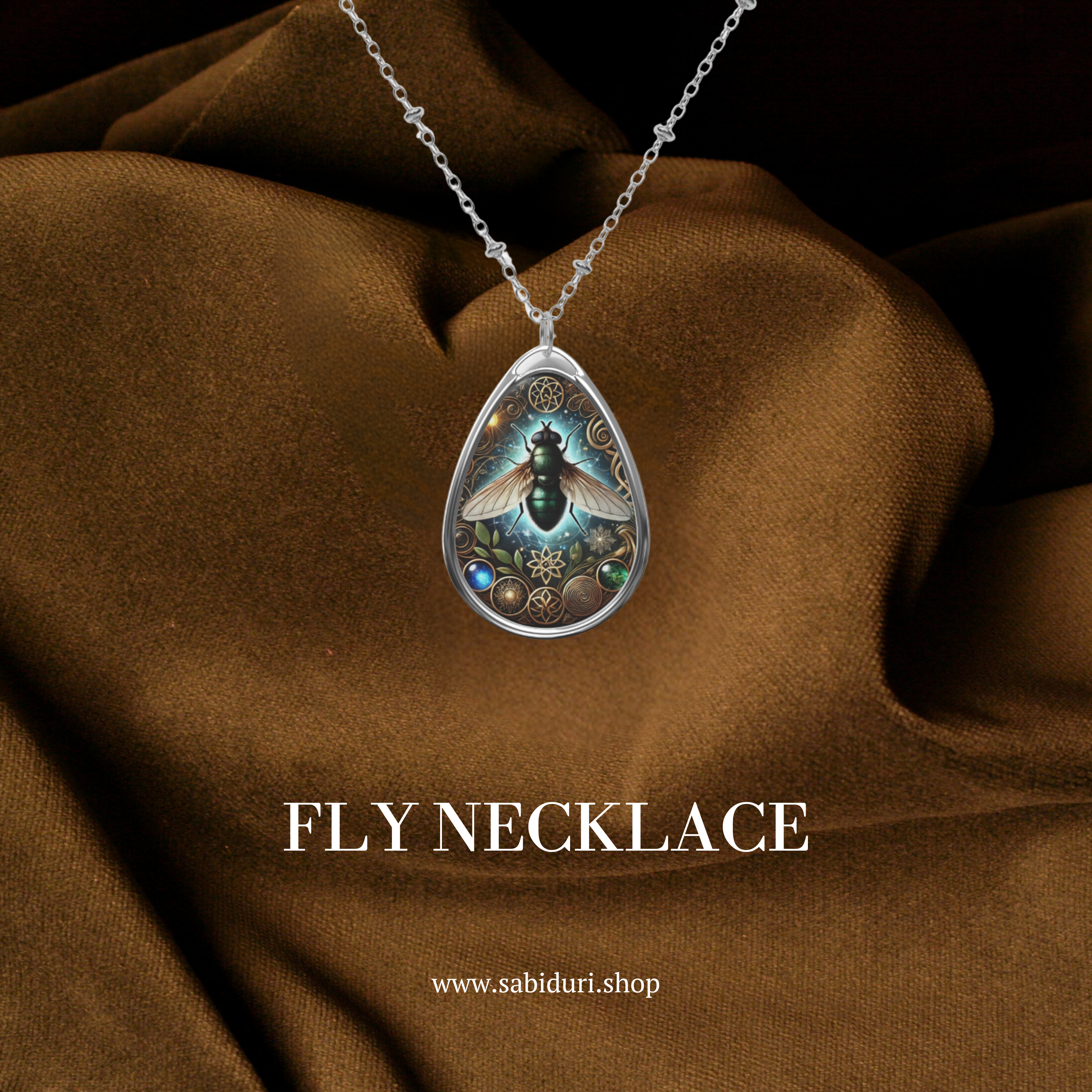 A silver teardrop pendant featuring an intricate illustration of a fly with glowing blue wings, surrounded by ornate golden patterns and small gemstones. The necklace is displayed against a rich brown fabric, with the words "FLY NECKLACE" and "www.sabiduri.shop" written in white.