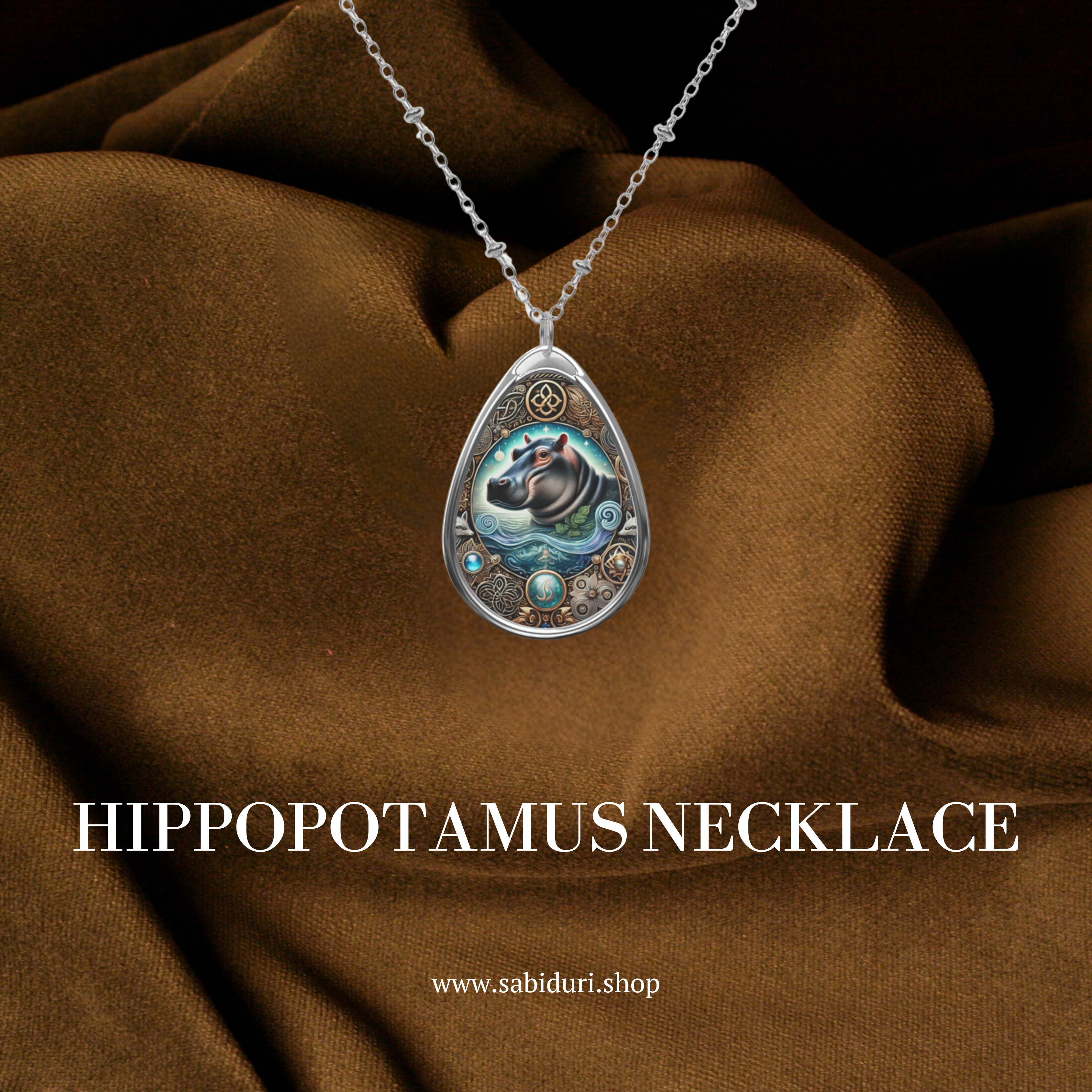 A close-up of the Hippopotamus Spirit Animal necklace, suspended over rich brown fabric. The pendant showcases a stylized hippo swimming in water with golden and blue embellishments, complemented by the text "Hippopotamus Necklace" and the website "www.sabiduri.shop."