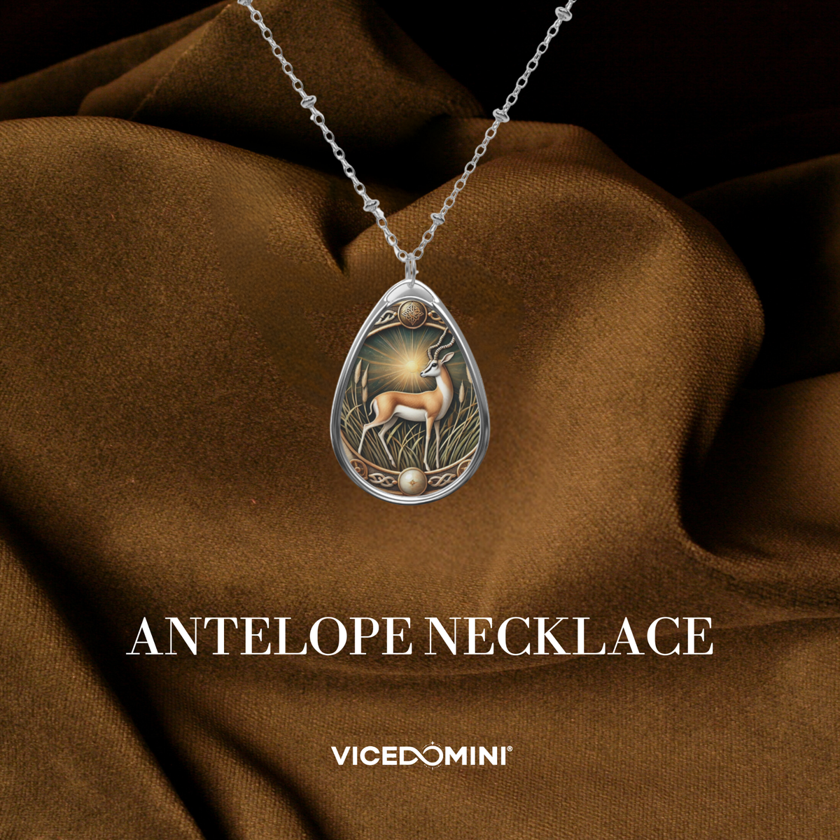 Silver teardrop pendant necklace featuring an engraved antelope and sun design, draped elegantly on brown satin fabric with 'ANTELOPE NECKLACE' and 'VICEDOMINI' text below.