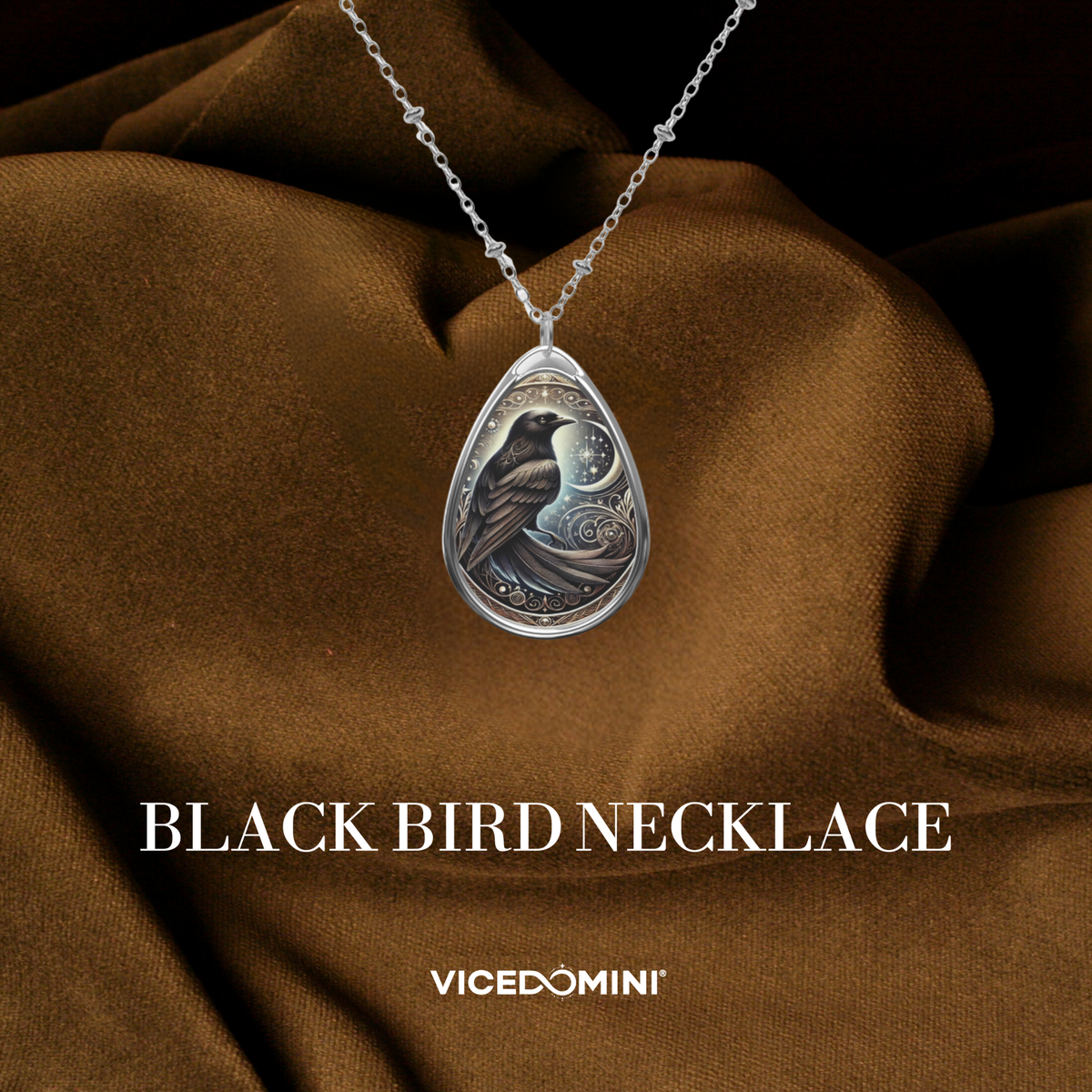 The Black Bird Spirit Animal Necklace elegantly laid on rich brown fabric, showcasing the pendant's intricate celestial detailing and deep-toned engraving of the bird. The words "Black Bird Necklace" and "VICEDOMINI" are included in the design.
