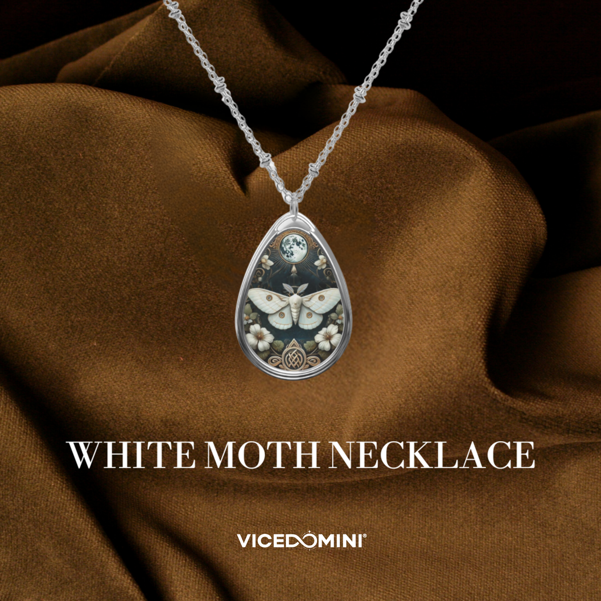 A teardrop-shaped pendant necklace featuring a white moth and floral design on a dark background, suspended from a silver chain and displayed against draped brown fabric. Text below reads 'WHITE MOTH NECKLACE' with the brand 'VICEDOMINI' at the bottom.