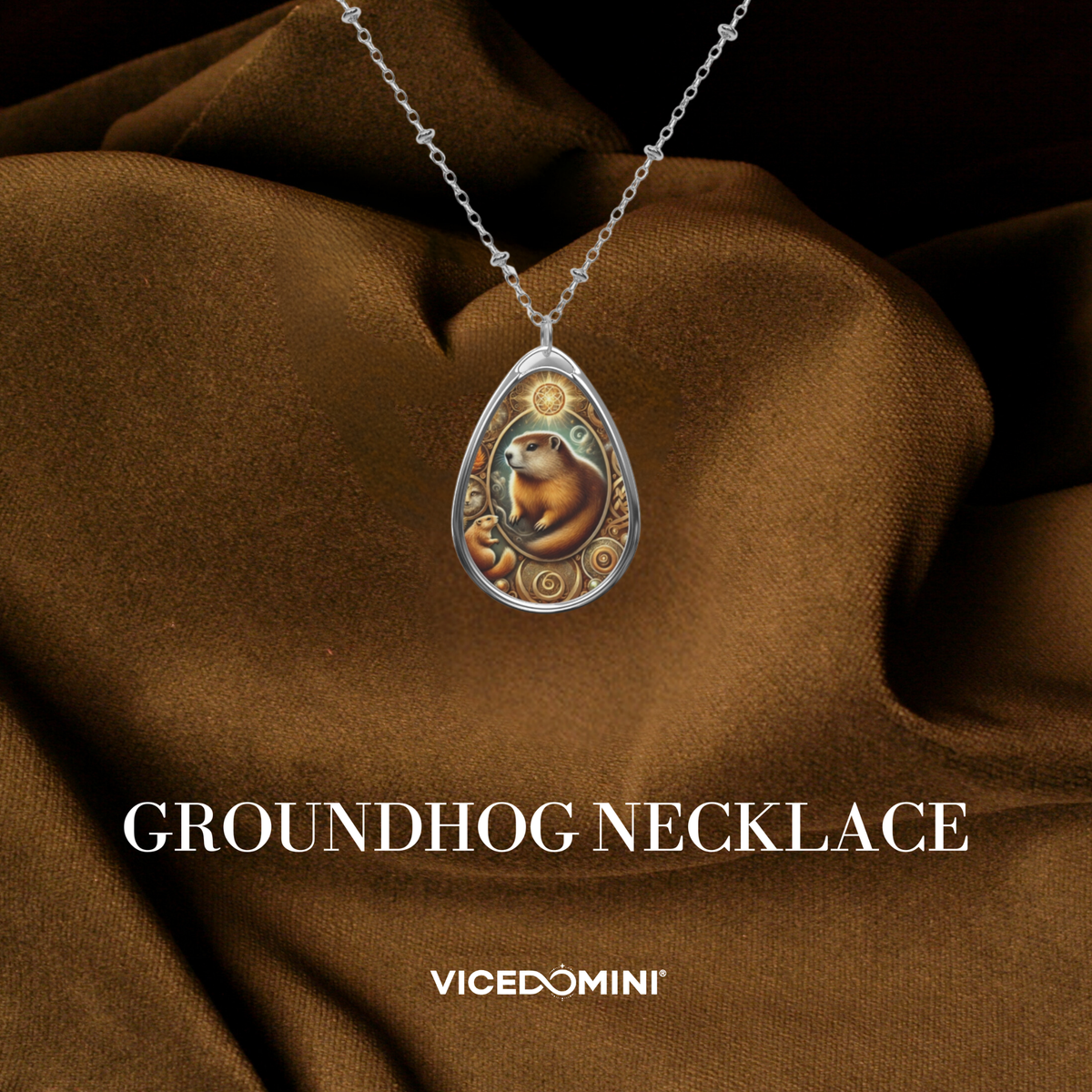 A teardrop-shaped pendant necklace featuring a groundhog illustration on a silver-toned chain, draped over brown satin fabric with the text 'GROUNDHOG NECKLACE' and 'VICEDOMINI' below.