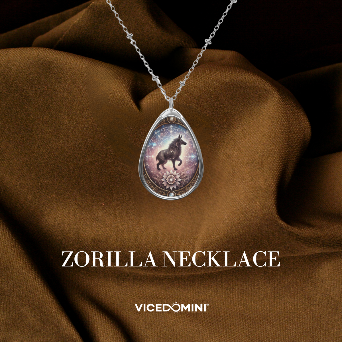 A teardrop-shaped silver pendant necklace featuring a colorful illustration of a black orca in a galaxy, displayed on draped brown satin fabric with the text 'ZORILLA NECKLACE' and 'VICEDOMINI' below.