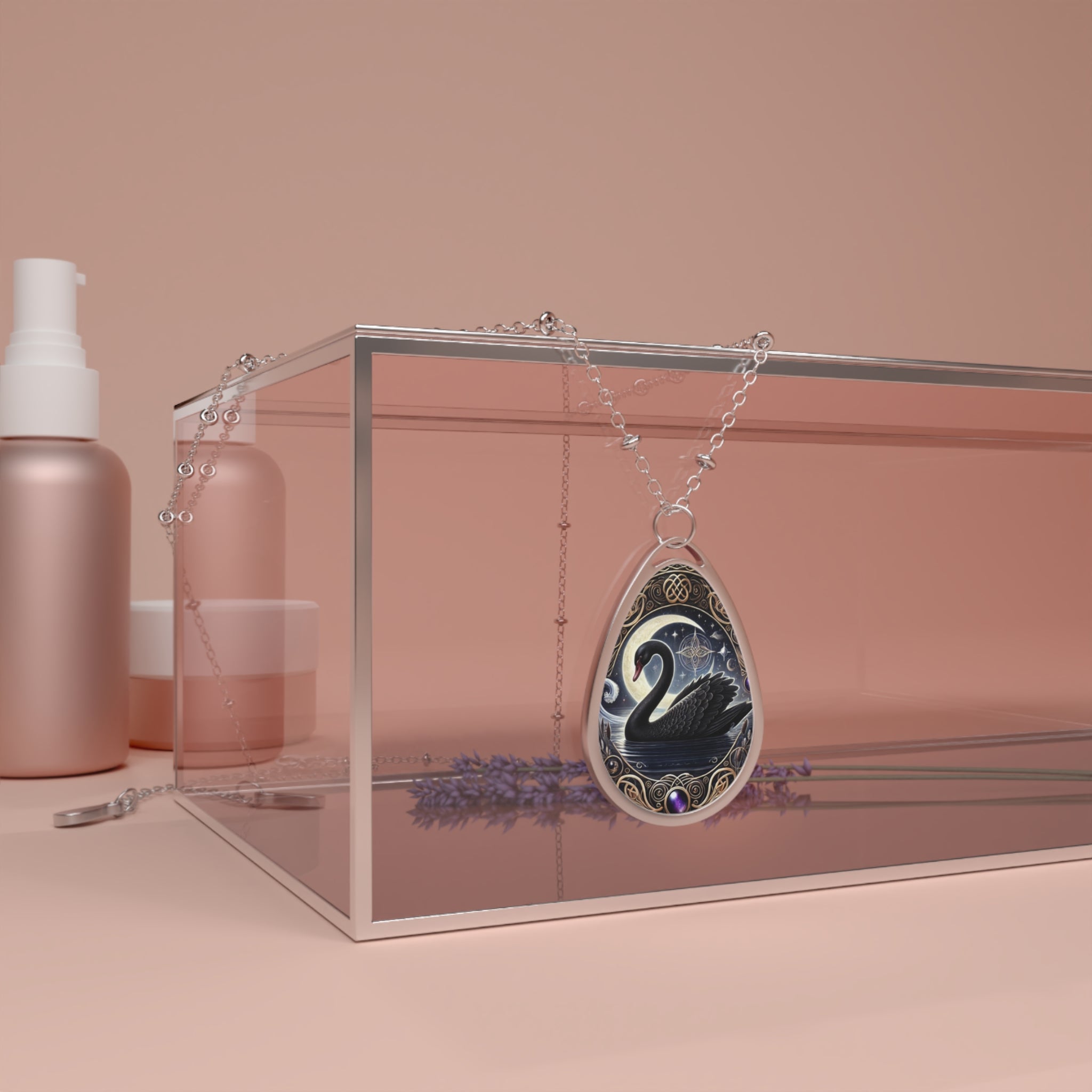 A teardrop-shaped pendant featuring a detailed illustration of a black swan gliding across a dark, moonlit lake, adorned with golden Celtic patterns and a deep purple gemstone at the bottom. The pendant hangs elegantly over a transparent jewelry box, surrounded by soft pink and neutral-toned cosmetic bottles.