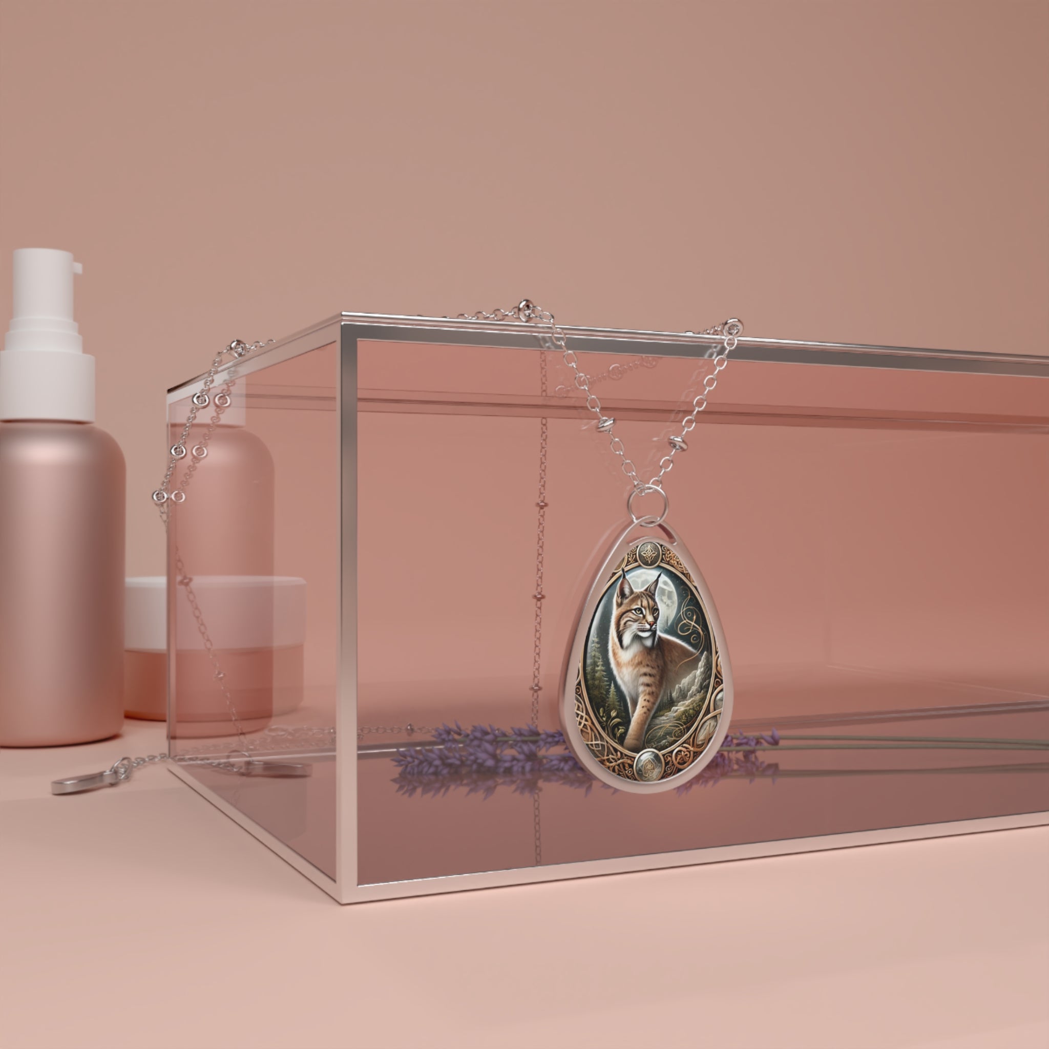 A teardrop-shaped pendant necklace featuring an intricately designed bobcat illustration with a mystical background. The pendant hangs elegantly on a silver chain, draped over a transparent display box, surrounded by soft pink and lavender-toned elements.