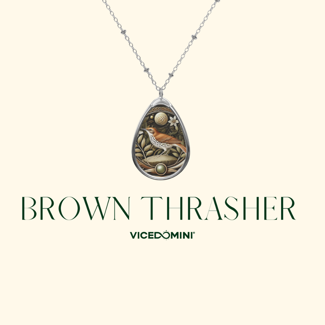 A teardrop-shaped pendant necklace with a silver-toned chain, featuring an intricate bird design in brown, gold, and white tones. The pendant is displayed against a light cream background with the text 'BROWN THRASHER' and 'VICEDOMINI' underneath.