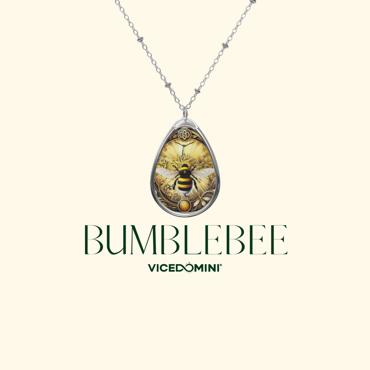 A silver teardrop pendant necklace featuring a detailed illustration of a bumblebee on a floral background, displayed on a light cream background with the brand name 'BUMBLEBEE' and sub-brand 'VICEDOMINI' printed below.