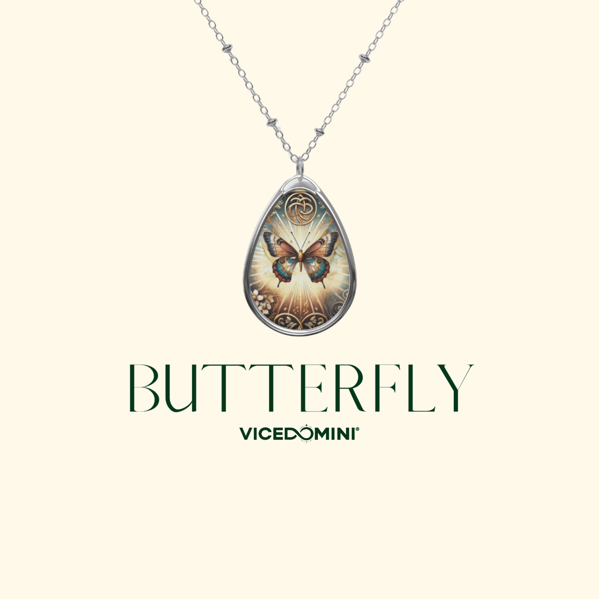 A silver teardrop pendant necklace featuring a detailed butterfly illustration with warm gold, orange, and blue tones, suspended from a delicate silver chain. The brand name 'VICEDOMINI' and the word 'BUTTERFLY' are printed below the pendant on a solid pale cream background.