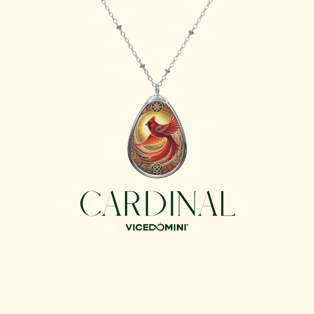 A silver teardrop pendant necklace featuring an illustrated cardinal bird on a warm gold and red background, displayed on a cream background with the brand name 'CARDINAL Vicedomini' below.