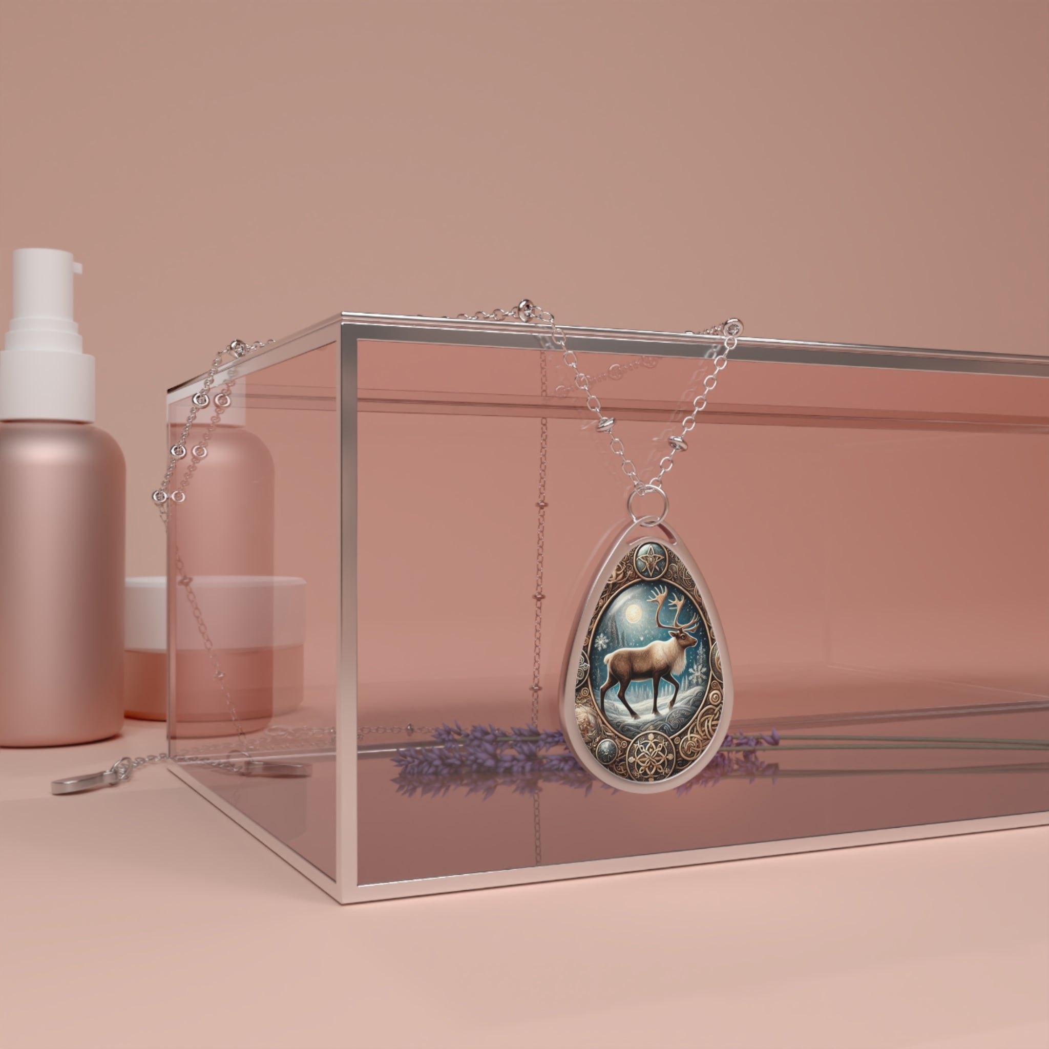 A teardrop-shaped pendant necklace featuring a detailed illustration of a caribou standing under a glowing moon and snowflakes. The pendant has intricate golden and blue accents and hangs over a transparent glass box with lavender flowers inside, set against a soft pink background.