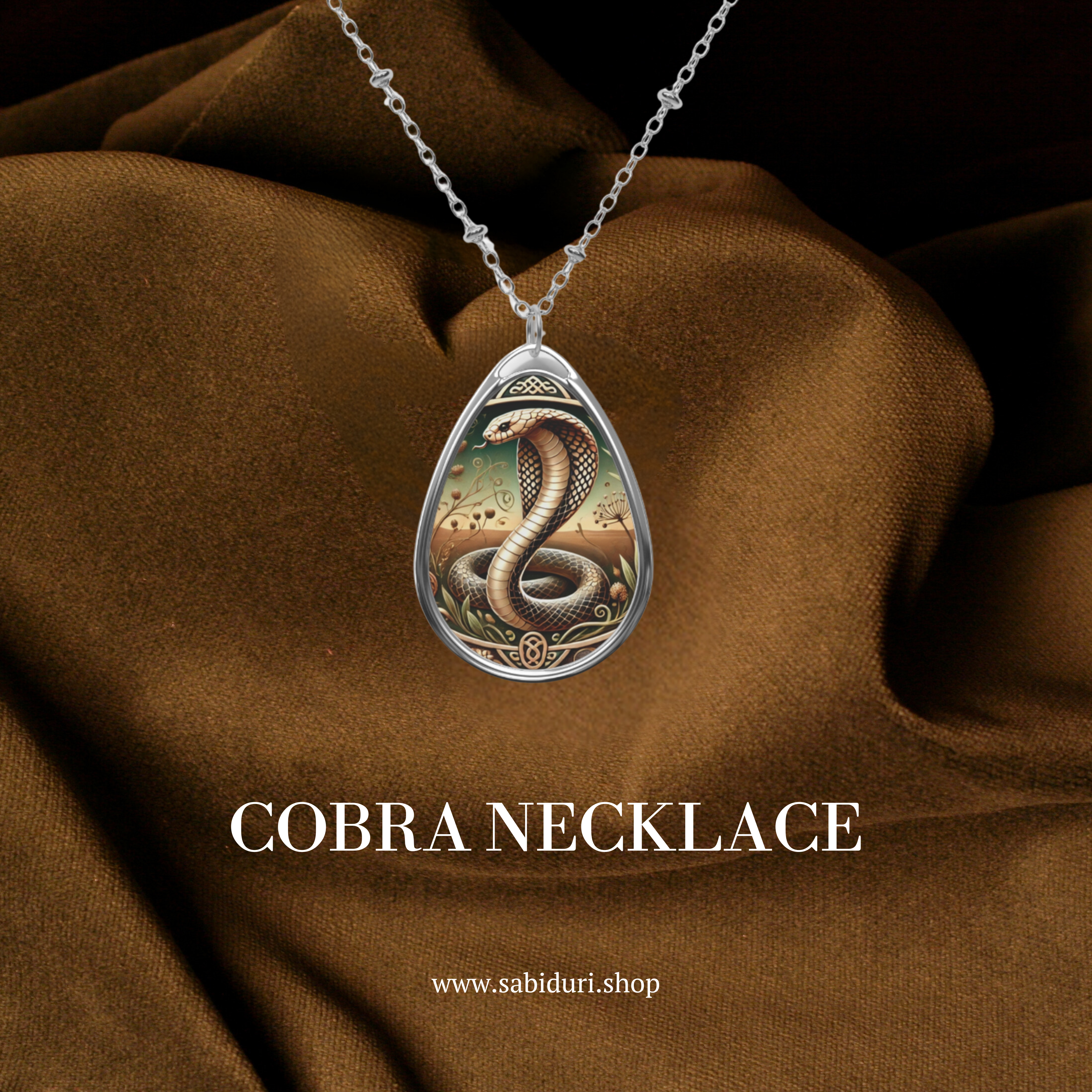 A cobra pendant necklace displayed on rich, dark brown fabric. The pendant depicts a coiled cobra with ornate surrounding designs, symbolizing protection and transformation. The text below reads "COBRA Necklace" along with the website "www.sabiduri.shop.