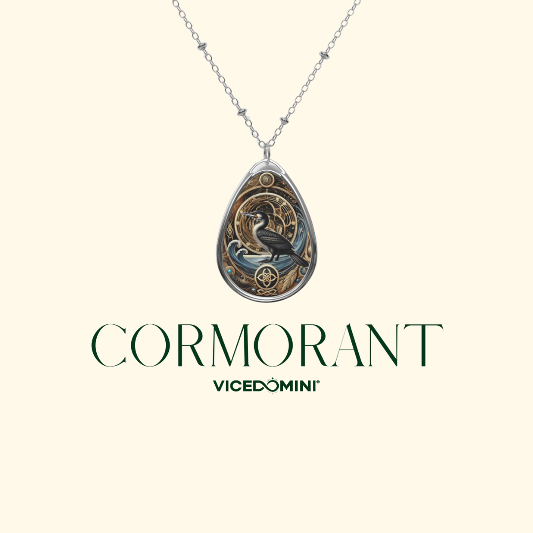 A silver-toned teardrop pendant necklace featuring an ornate bird design with gold, blue, and black details, suspended from a delicate chain on a light cream background. Below the necklace, the text 'CORMORANT' and 'VICEDOMINI' are displayed.