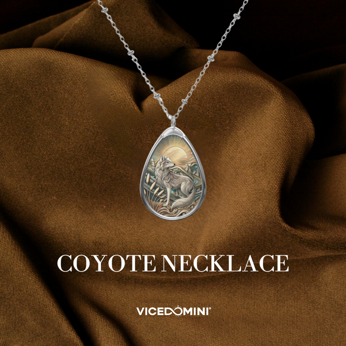 A teardrop-shaped silver pendant necklace featuring an engraved coyote and moon design, displayed on draped brown fabric with the text 'COYOTE NECKLACE' and 'VICEDOMINI' below.