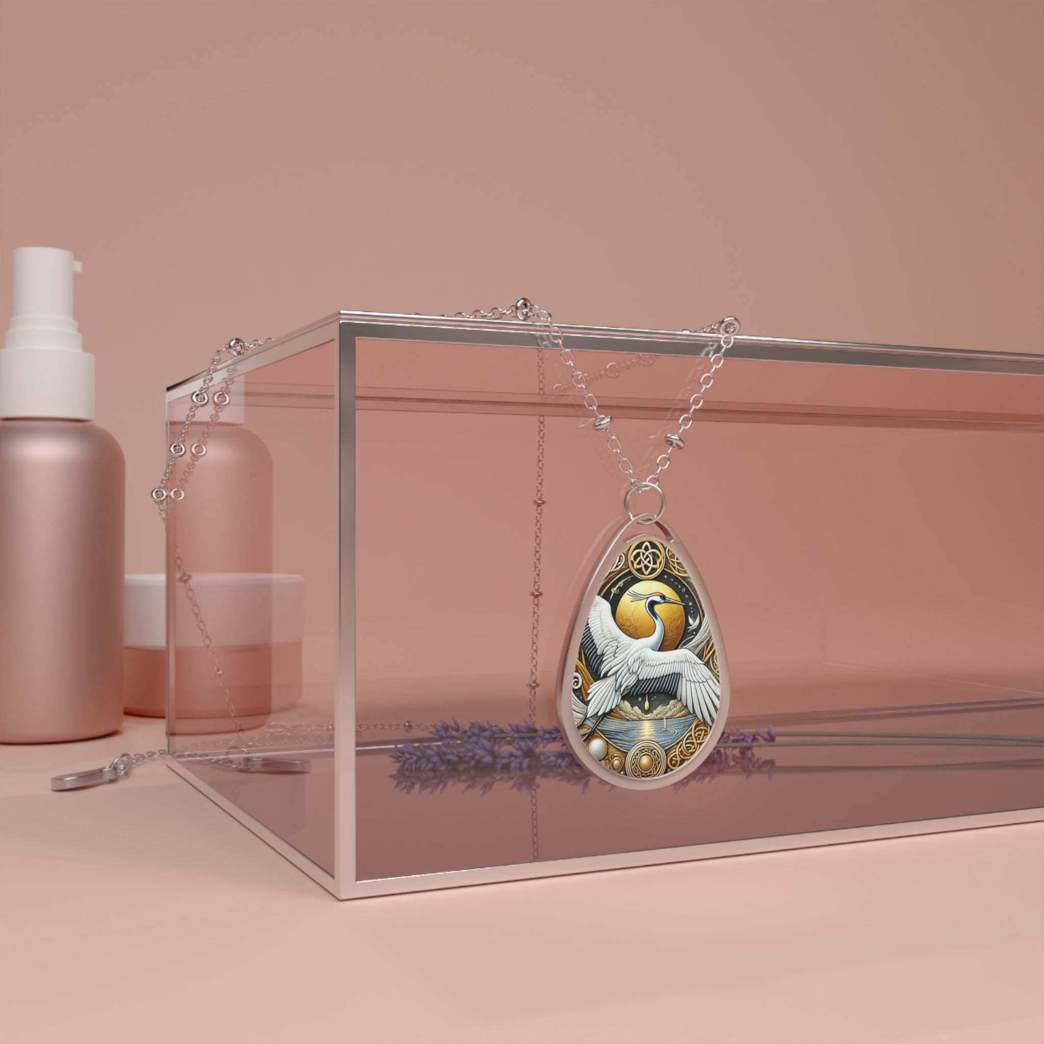 A silver chain necklace with a teardrop-shaped pendant featuring an intricate illustration of a white crane in flight against a golden sun, surrounded by ornate metallic details. The necklace is elegantly draped over a transparent glass box with lavender sprigs underneath, set against a soft pink background.