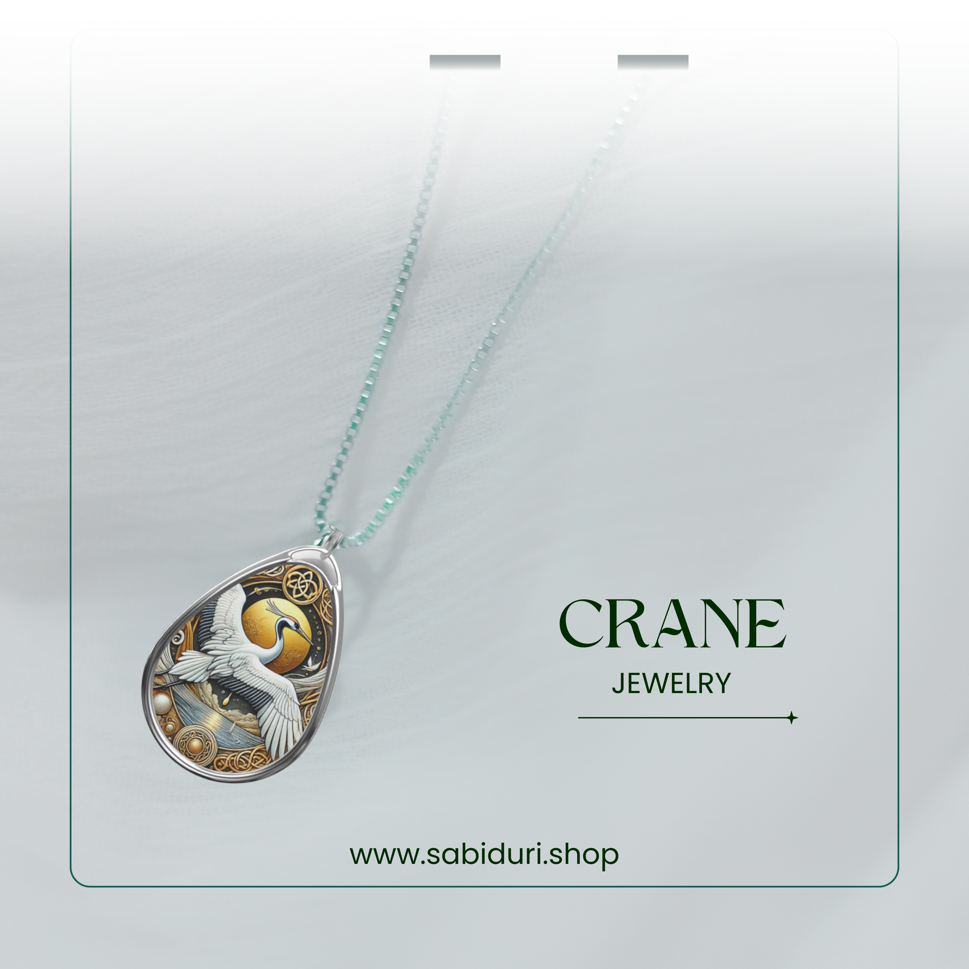 The Crane Necklace is displayed against a soft white-to-transparent gradient background. The teardrop-shaped pendant features a white crane soaring across a golden celestial scene with delicate filigree detailing. The text "CRANE JEWELRY" and "www.sabiduri.shop" accompany the image, reinforcing its branding.