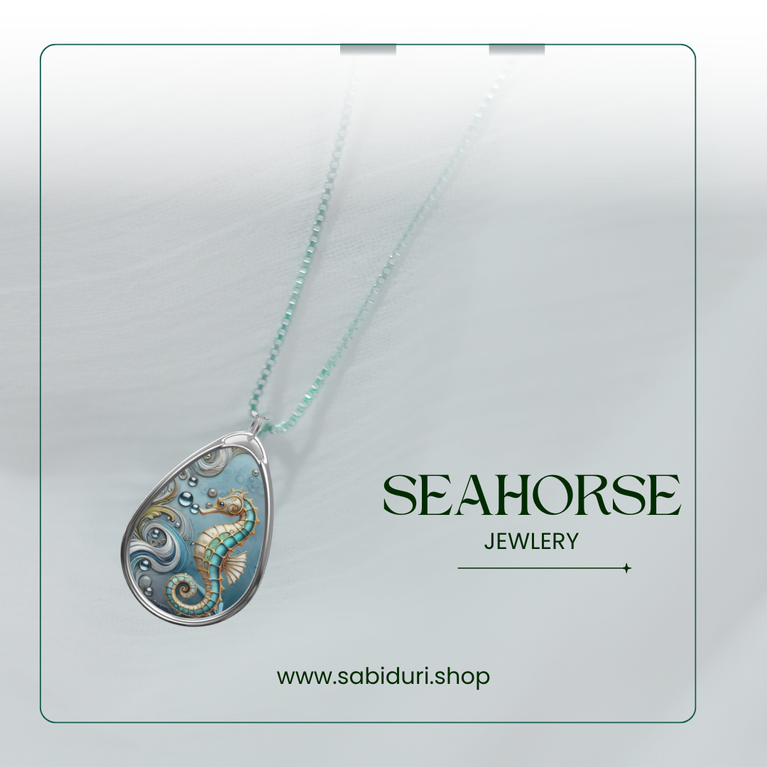 A silver necklace with a teardrop pendant featuring a detailed seahorse and ocean wave design in blue and gold, shown against a white background. The text "Seahorse Jewelry" and "www.sabiduri.shop" are displayed at the bottom in green.