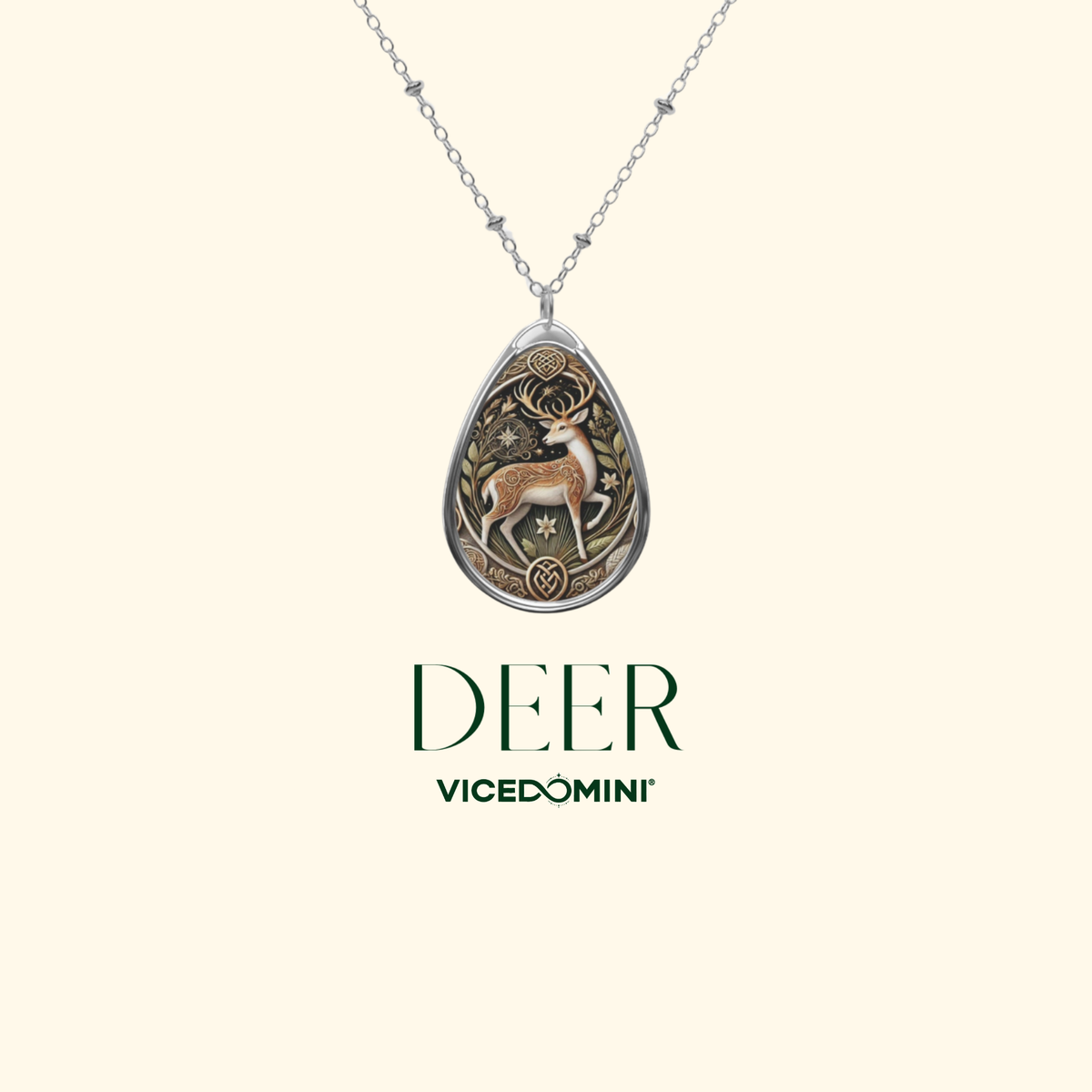 A silver teardrop pendant necklace featuring an engraved deer design with warm metallic detailing, shown against a light cream background with the text 'DEER VICEDOMINI' below.