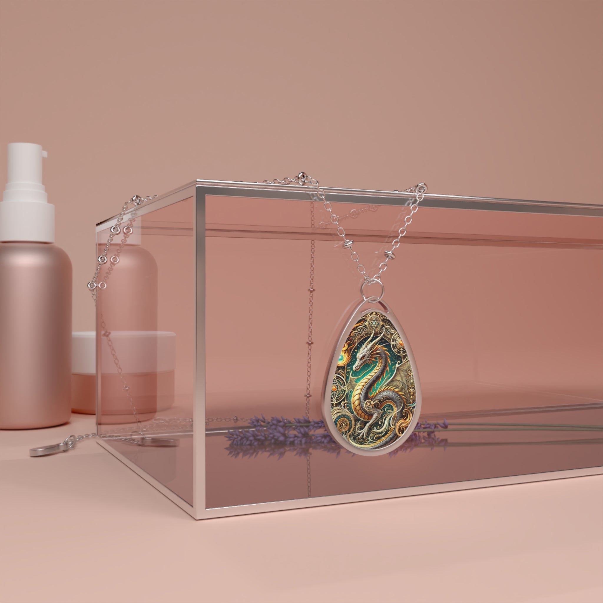 A teardrop-shaped pendant with an intricate dragon design, featuring swirling golden and emerald-green details. The pendant hangs from a delicate silver chain, draped over a transparent box with a soft pink background. Beauty products and dried lavender sprigs add to the elegant display.