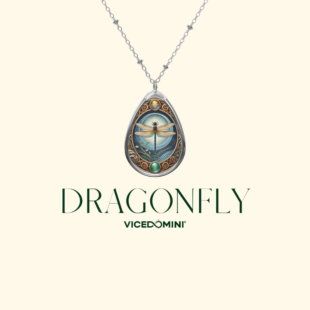 A teardrop pendant necklace with a silver-toned chain and a detailed dragonfly illustration in the center, displayed on a light cream background with the text 'DRAGONFLY' and 'VICEDOMINI' below.