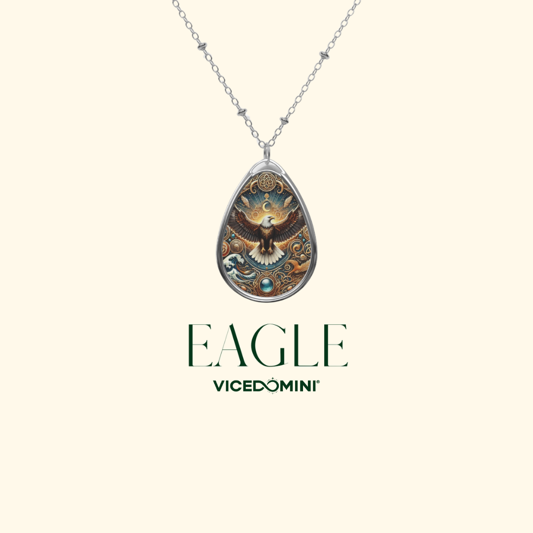 A silver teardrop pendant necklace featuring an intricate eagle illustration with gold, brown, and blue details, shown against a light cream background with the text 'EAGLE VICEDOMINI' below.