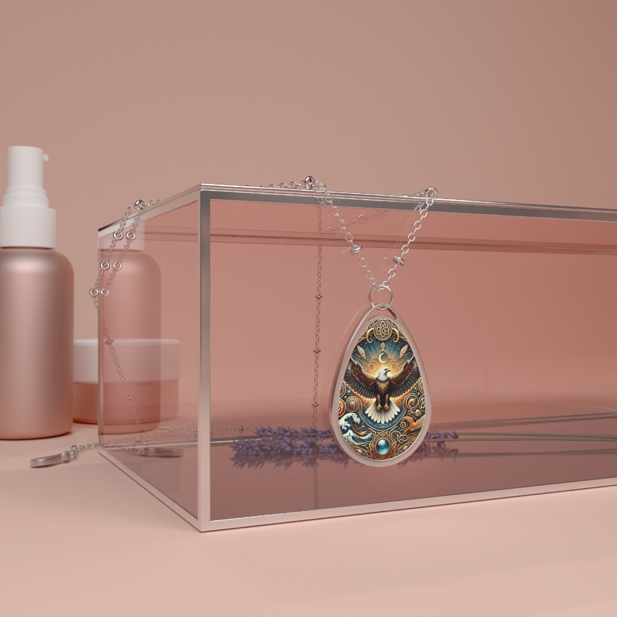 A teardrop-shaped pendant necklace featuring an intricately designed eagle with outstretched wings, surrounded by celestial patterns and a glowing sun, resting on a glass box. The chain drapes elegantly over the edges, with a soft pastel-toned background.