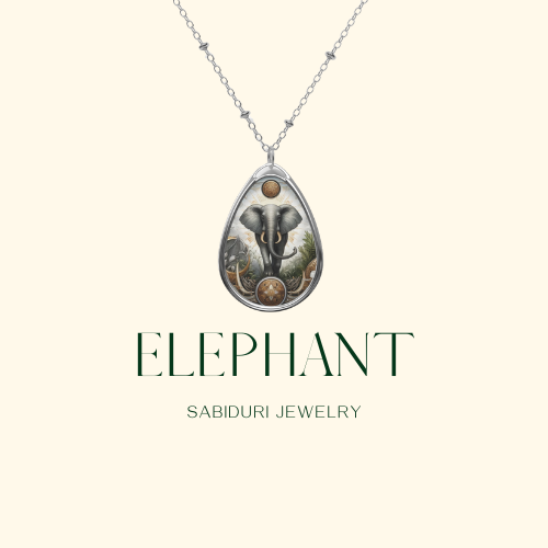 A silver necklace featuring a pendant of a majestic elephant surrounded by intricate patterns and earthy designs, displayed on a minimalist cream background. The text reads "ELEPHANT Sabiduri Jewelry.