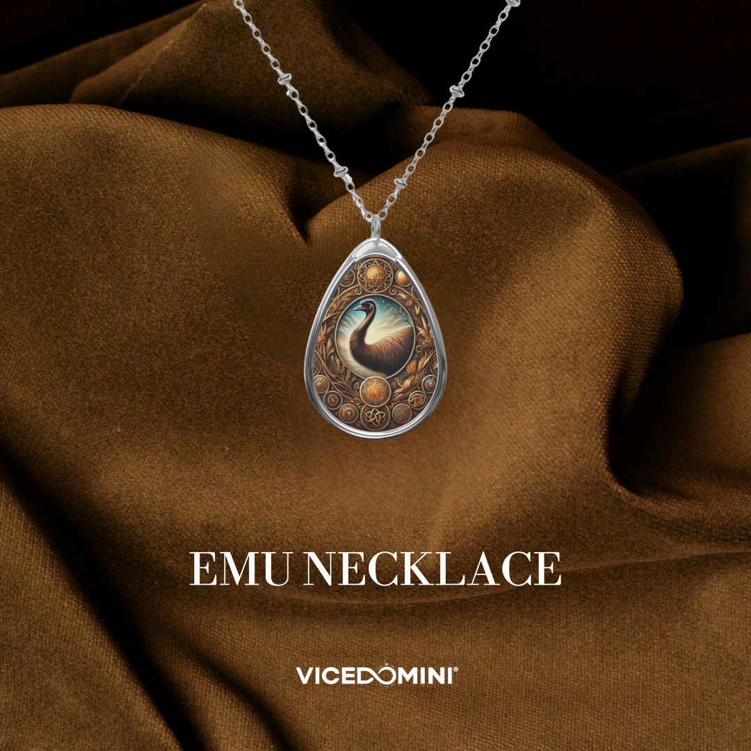 A teardrop-shaped silver pendant necklace featuring an intricate emu illustration, draped over brown satin fabric. The text 'EMU NECKLACE' and the brand 'VICEDOMINI' are displayed below.