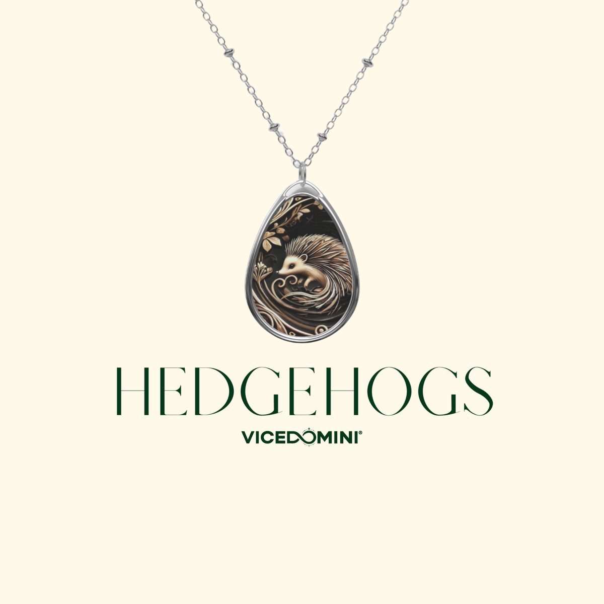 A teardrop-shaped pendant necklace featuring a detailed hedgehog illustration in gold and black, suspended from a silver chain. The brand name 'HEDGEHOGS' and sub-brand 'VICEDOMINI' are printed below the pendant on a solid pale cream background.