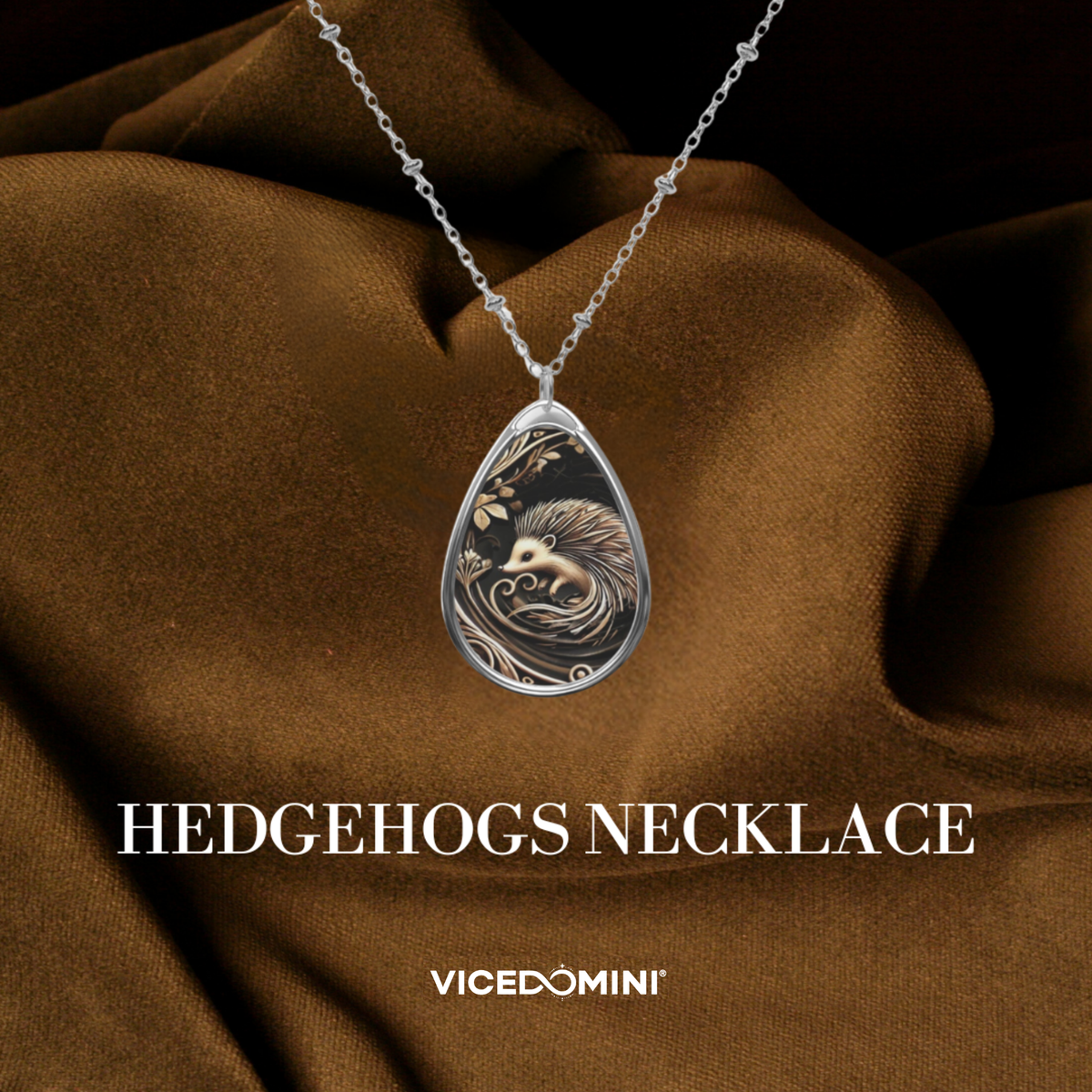 A silver teardrop pendant necklace featuring an engraved hedgehog design, displayed against a draped brown fabric background with text overlays reading 'HEDGEHOGS NECKLACE' and 'VICEDOMINI'.