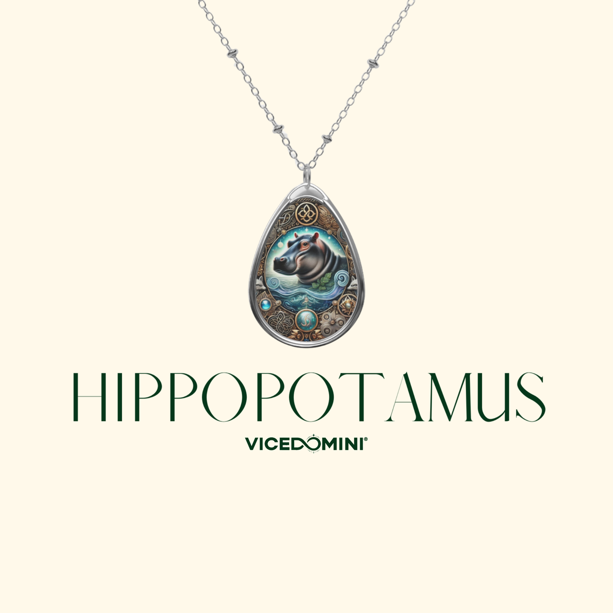 A teardrop-shaped pendant necklace featuring an illustrated hippopotamus design with turquoise, gold, and dark blue details, suspended from a silver-toned chain. The brand name 'VICEDOMINI' and the word 'HIPPOPOTAMUS' are printed below on a light cream background.