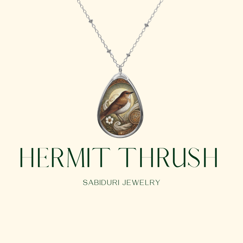 A delicate silver necklace with a teardrop-shaped pendant showcasing a hermit thrush bird, surrounded by floral and Celtic-inspired engravings. The pendant is displayed on a soft, neutral background, with the text "HERMIT THRUSH" and "SABIDURI JEWELRY" elegantly positioned beneath.