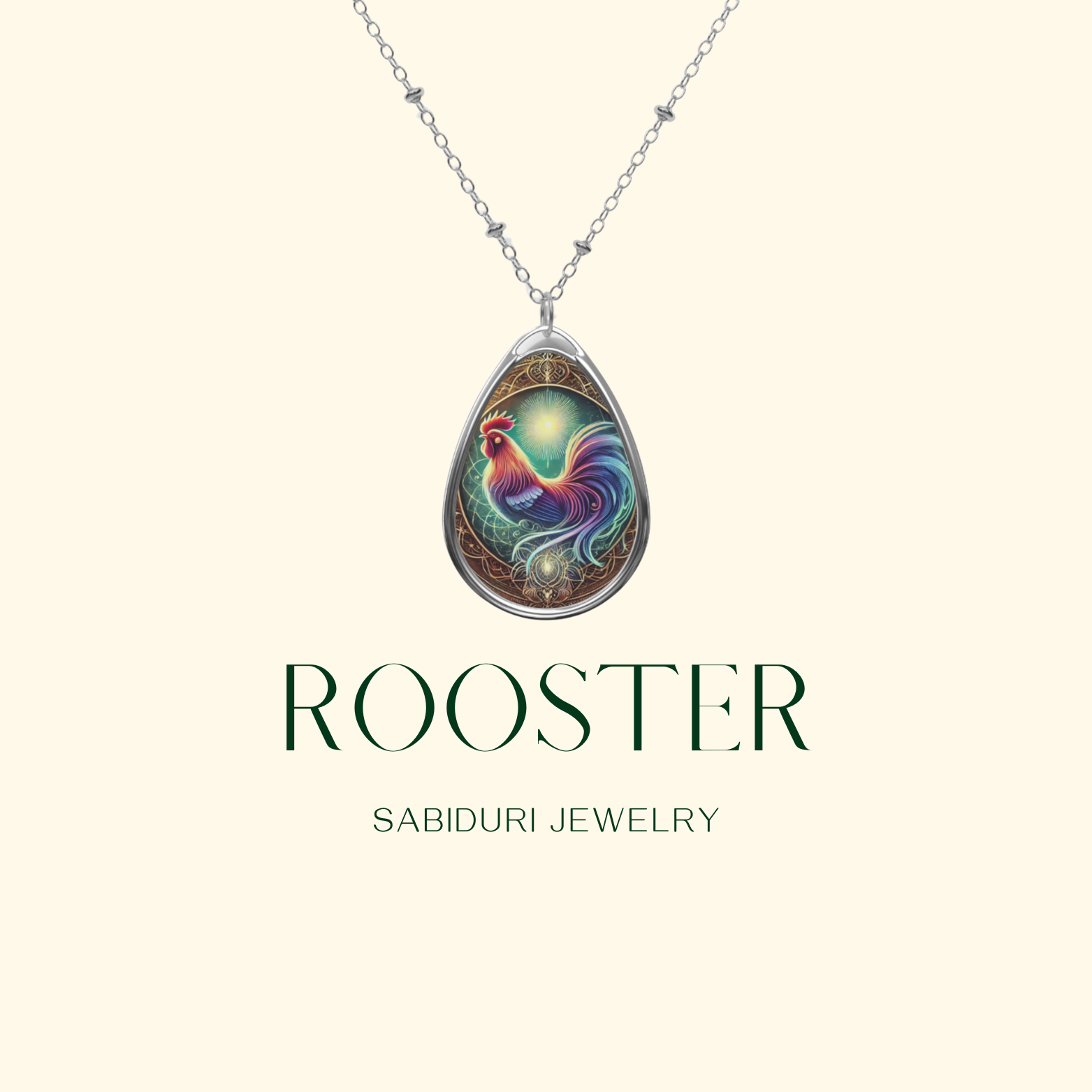 A rooster-themed teardrop pendant necklace is displayed on a plain beige background. The necklace has an ornate, celestial-inspired design, with a colorful rooster in the center. Below, the words "ROOSTER" and "SABIDURI JEWELRY" are written in elegant typography.