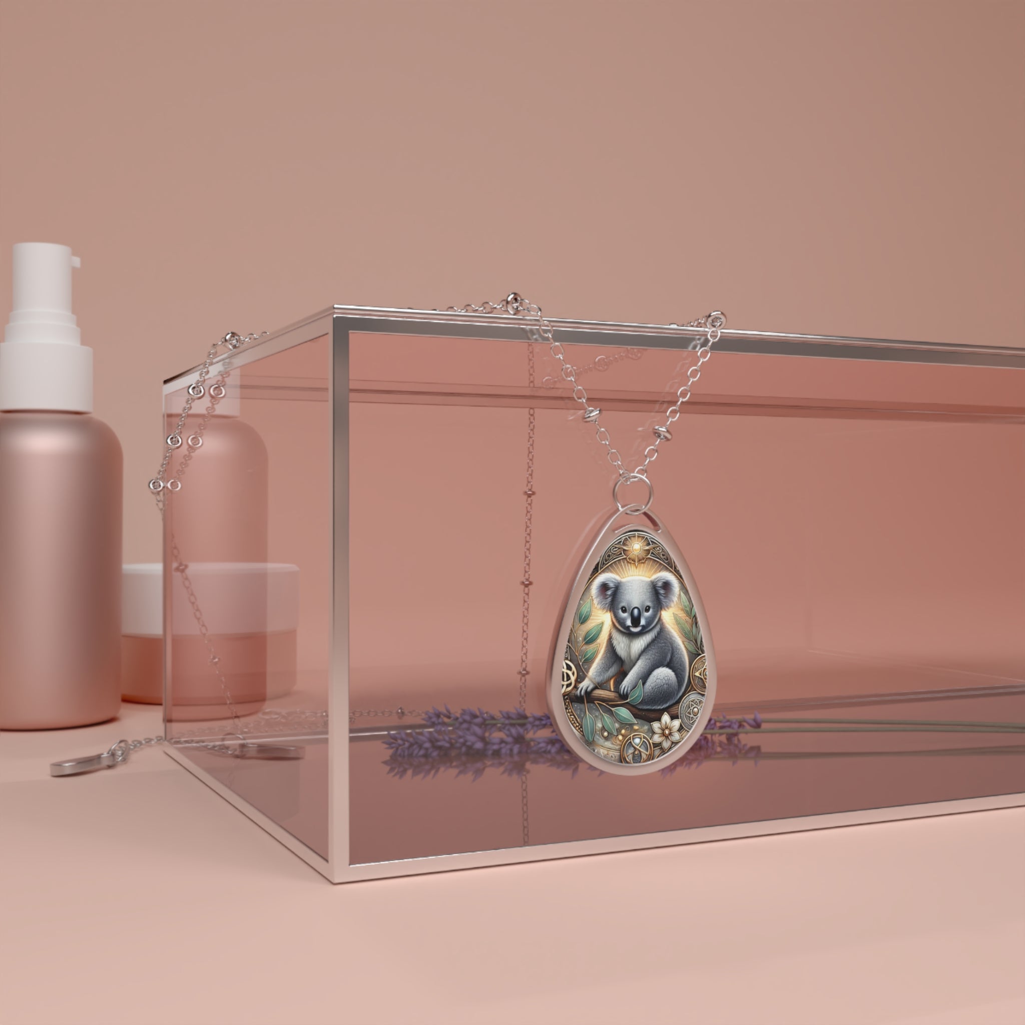 The Koala necklace elegantly draped over a transparent glass box, surrounded by subtle natural elements and a soft pink-beige background. The pendant’s koala artwork is detailed with earthy and celestial elements.