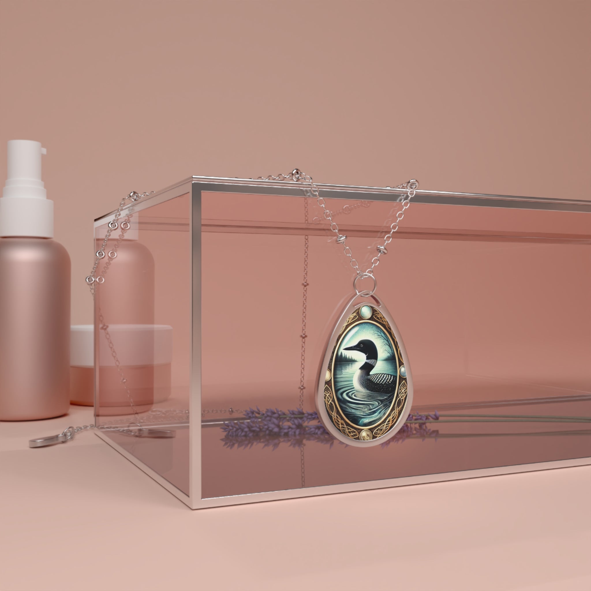 The Loon pendant is draped over a clear acrylic box with soft pink and lavender hues in the background. The necklace’s chain elegantly cascades over the box, emphasizing the detailed artwork of the loon swimming in a moonlit lake, surrounded by ornate gold detailing.