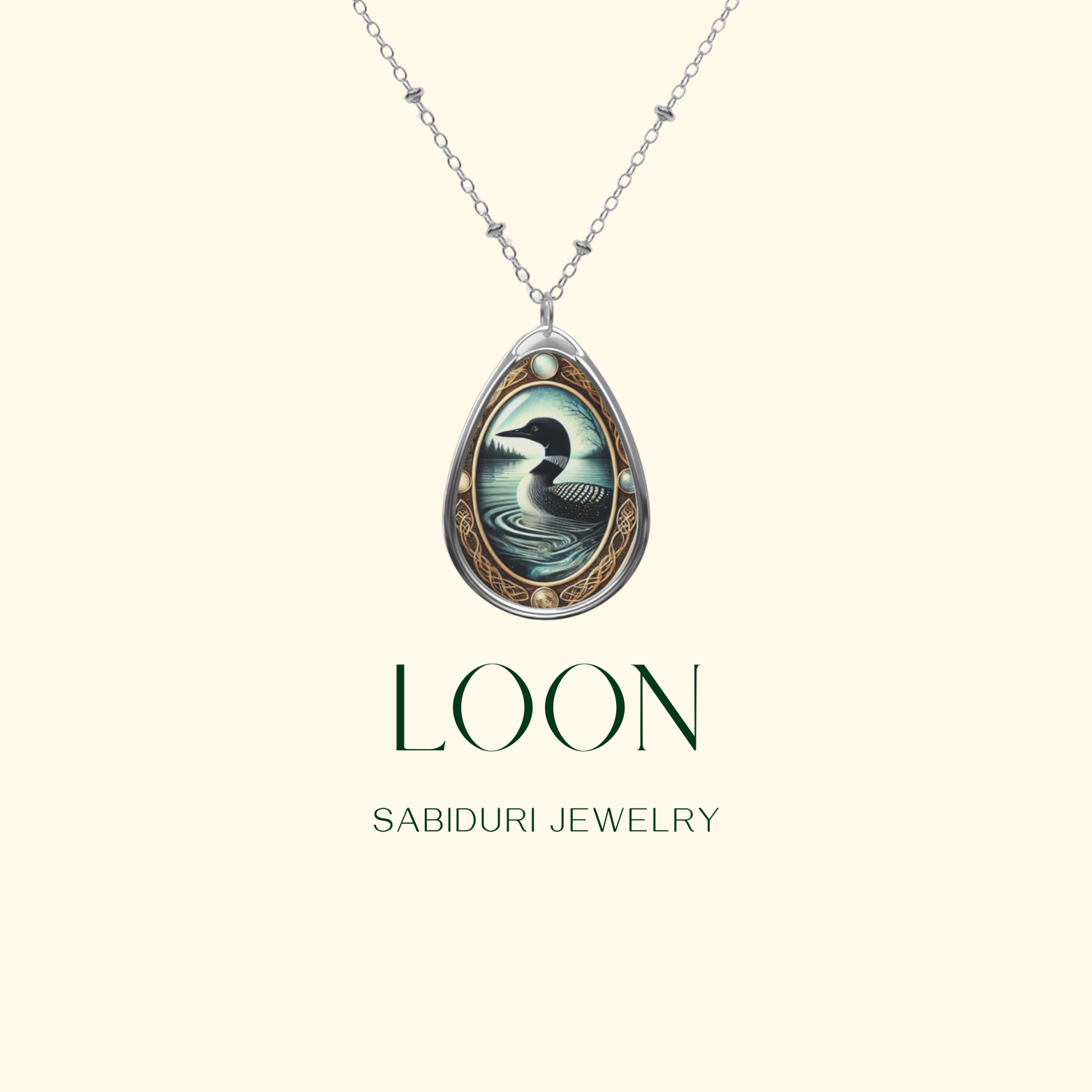 A silver teardrop-shaped pendant features an intricate illustration of a loon swimming in a calm lake, encircled by a delicate gold frame with celestial and natural elements. Below, "LOON" and "SABIDURI JEWELRY" are written in elegant typography on a soft beige background.