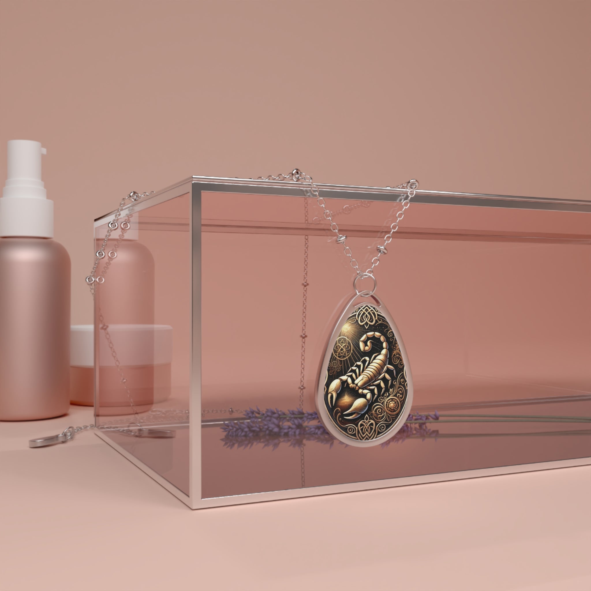 A silver chain necklace with a teardrop-shaped pendant featuring an intricately engraved scorpion design in gold and black tones. The pendant is elegantly draped over a modern transparent jewelry box, with soft pink beauty product containers and sprigs of lavender in the background.