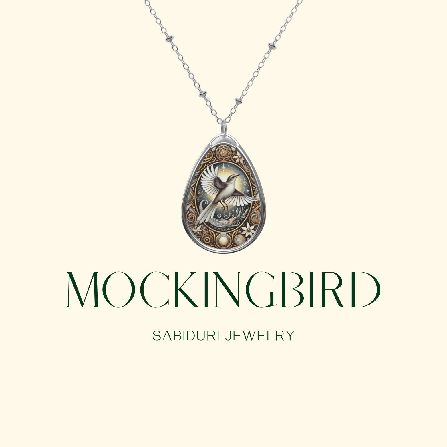 A teardrop-shaped pendant featuring an intricately designed mockingbird in mid-flight, surrounded by golden filigree and delicate floral patterns. The necklace is displayed on a beige background with "Mockingbird" and "Sabiduri Jewelry" written below.